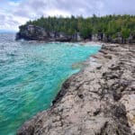 Indian Head Cove - a rocky cliff along a bay with bright turquoise water, and forest in the background.