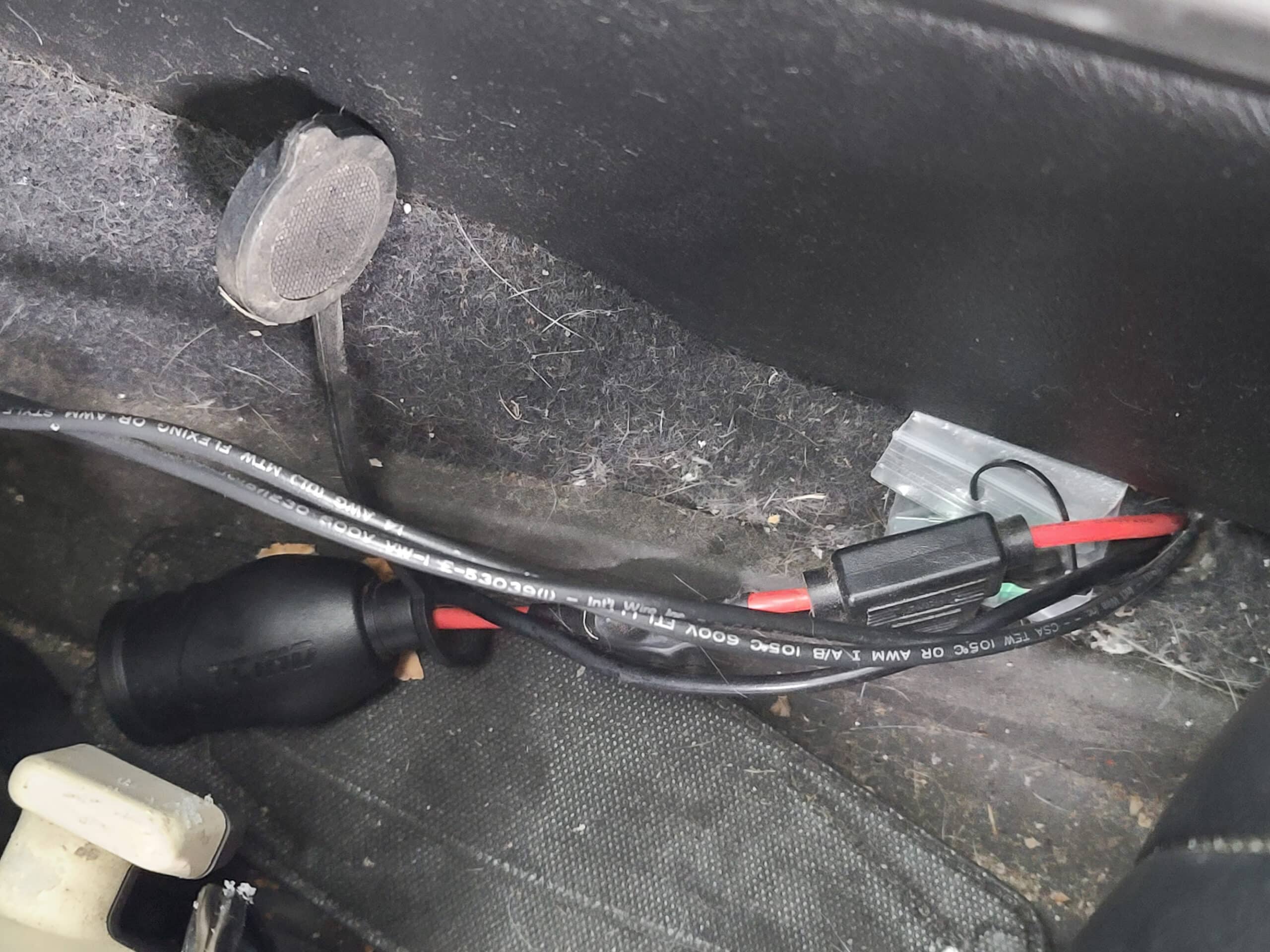 A 12v power port and two wires next to the driver's seat in a car.