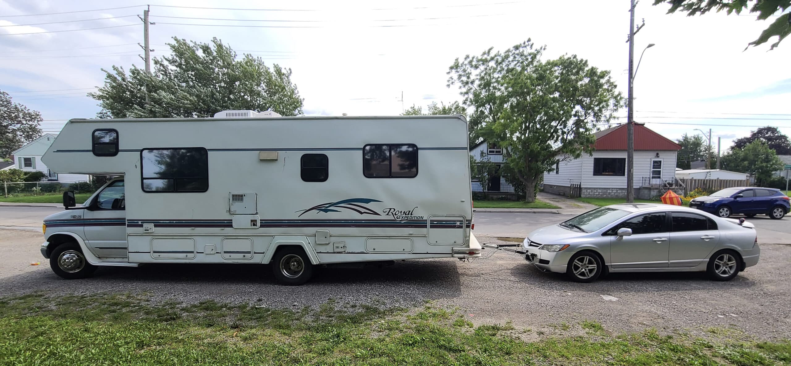 A side view of a motorhome with a car behind it, connected by a tow bar.