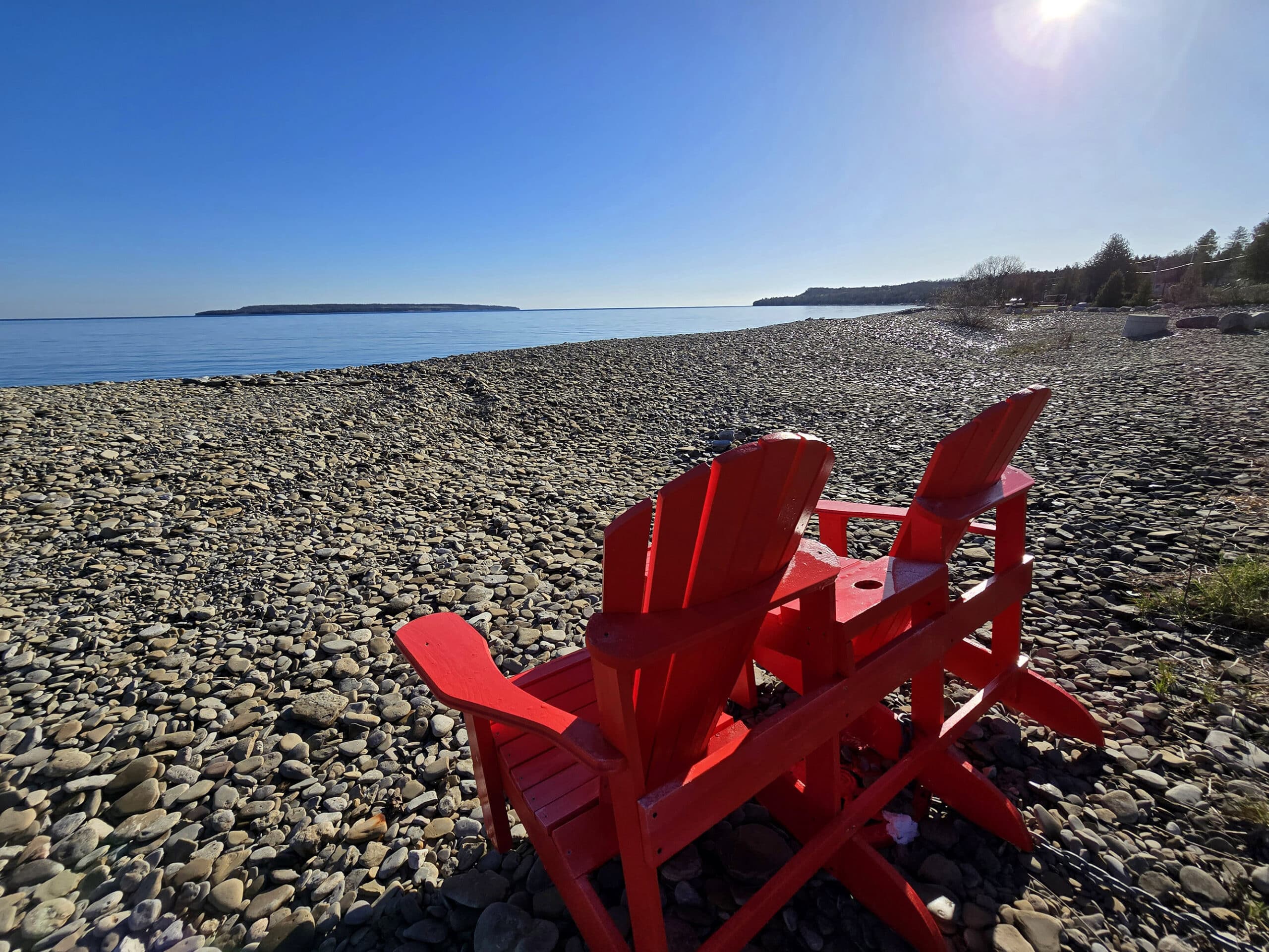 2 red Muskoka chairs overlooking Big Bay, on a rocky beach.