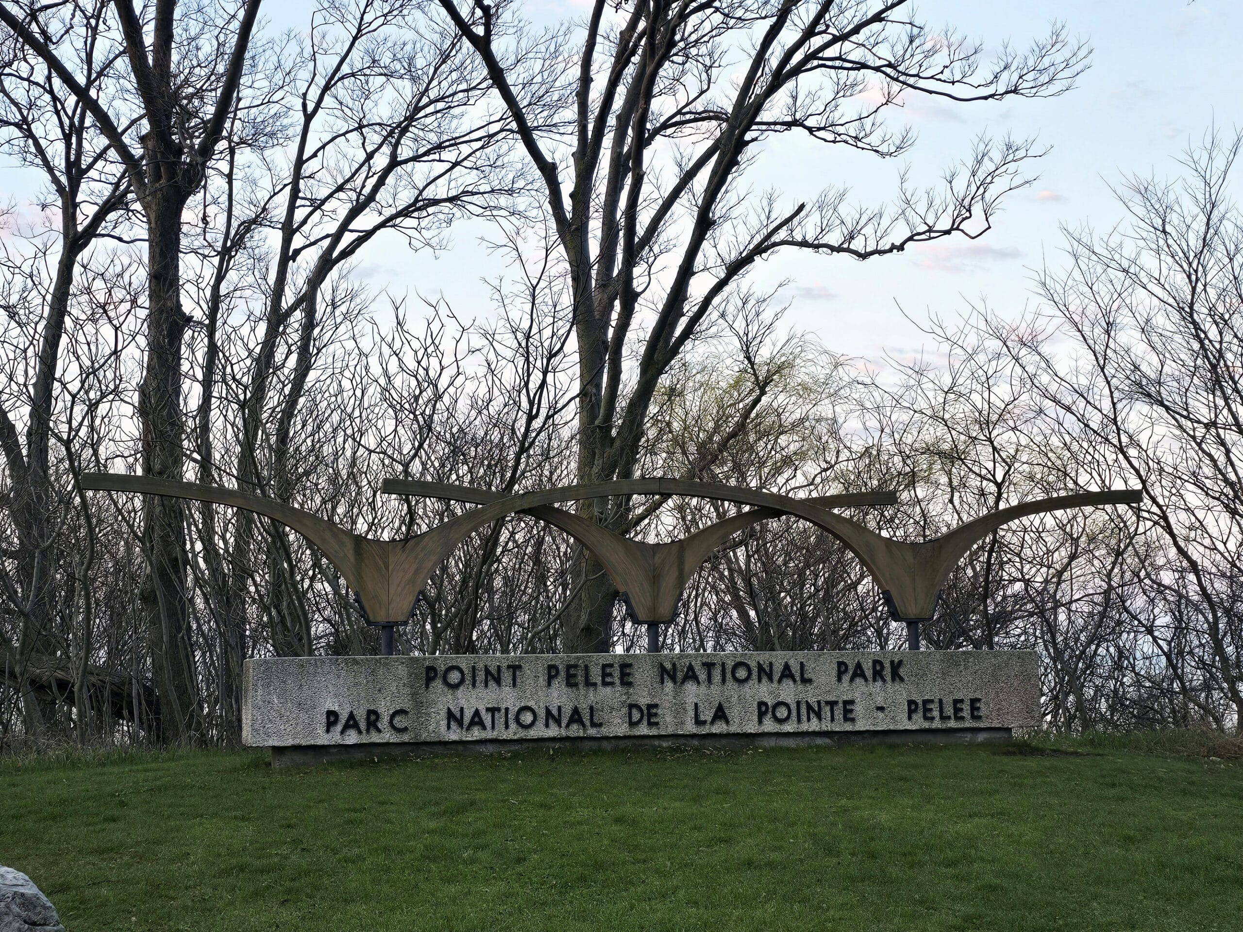 A concrete sign at the opening of the park.  3 stylized geese appear to fly over a sign that says point pelee national park.