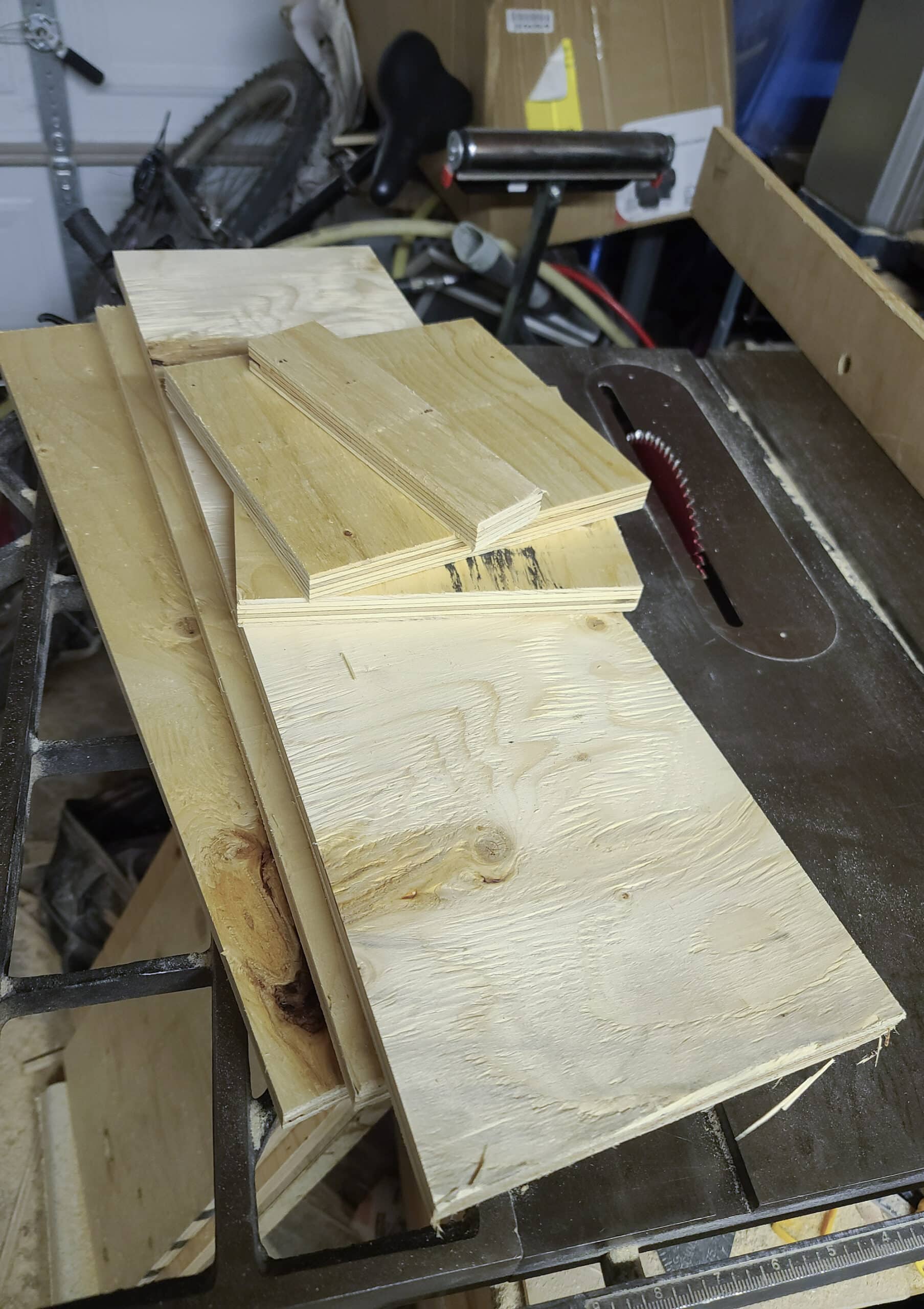 A small pile of cut out plywood boards on top of a table saw.