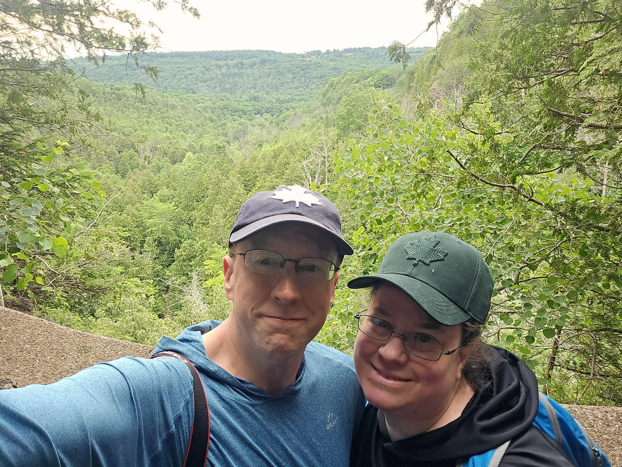 A middle aged couple standing over the Eugenia Falls gorge, with a valley in the background.