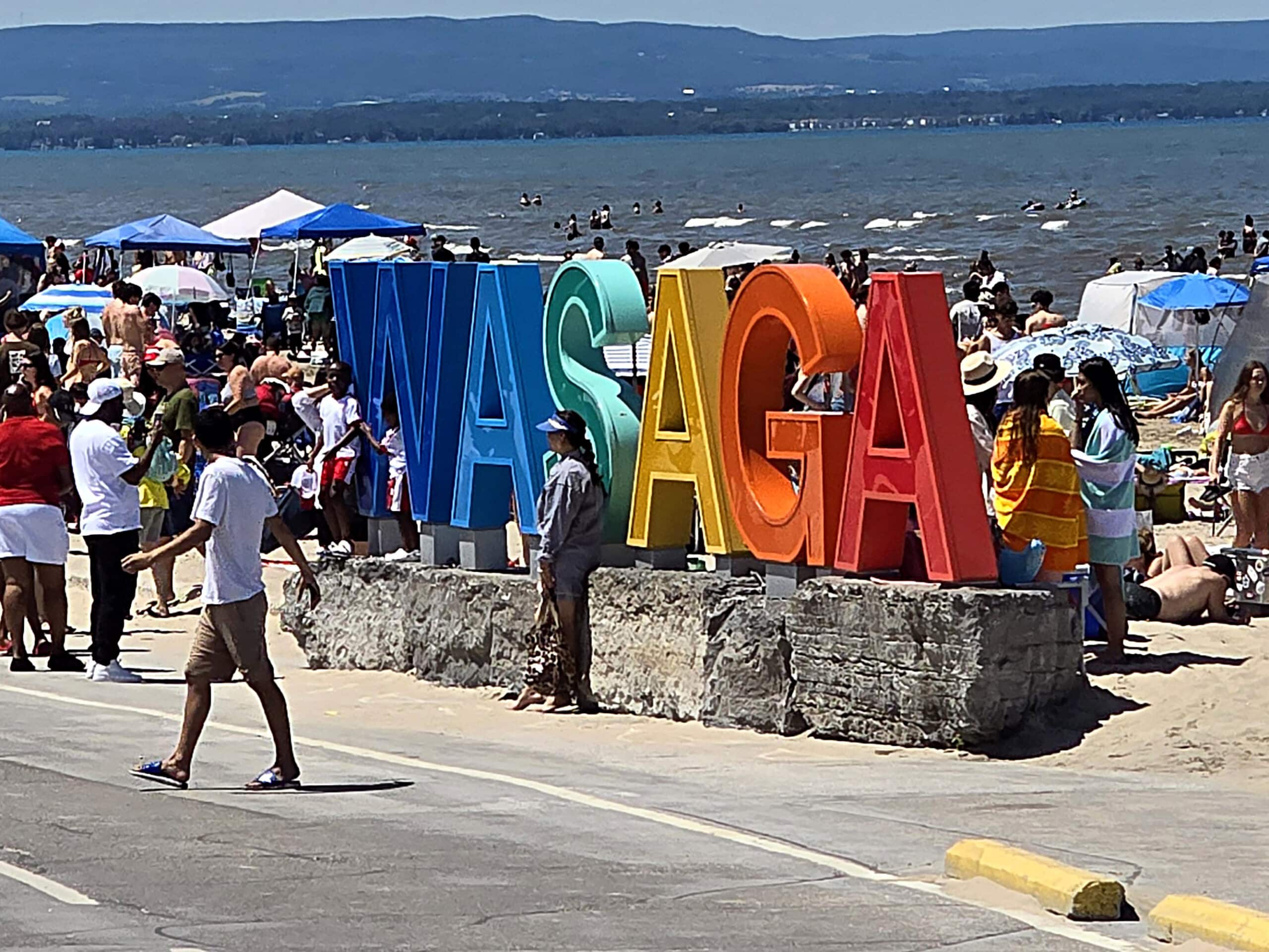 A rainbow sign that says wasaga, surrounded by people.