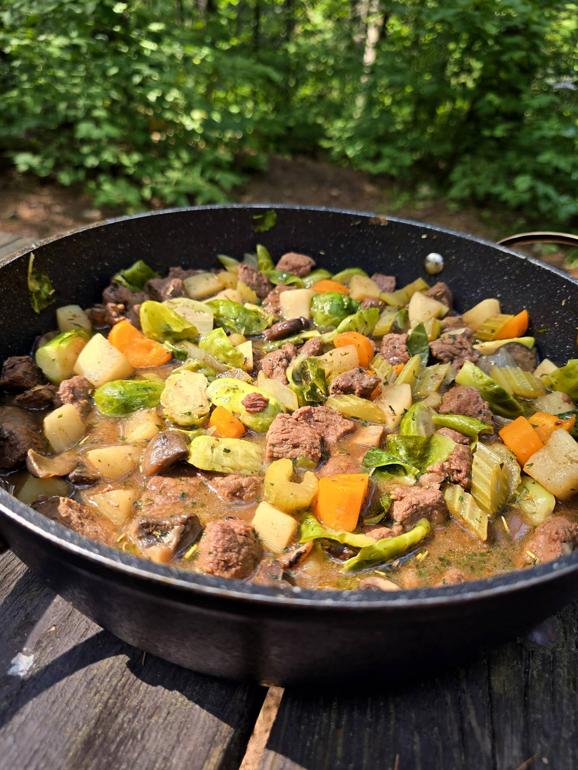 A large pot of campfire stew over a charcoal BBQ.