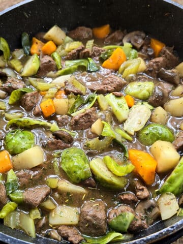 A large pot of campfire stew over a charcoal BBQ.