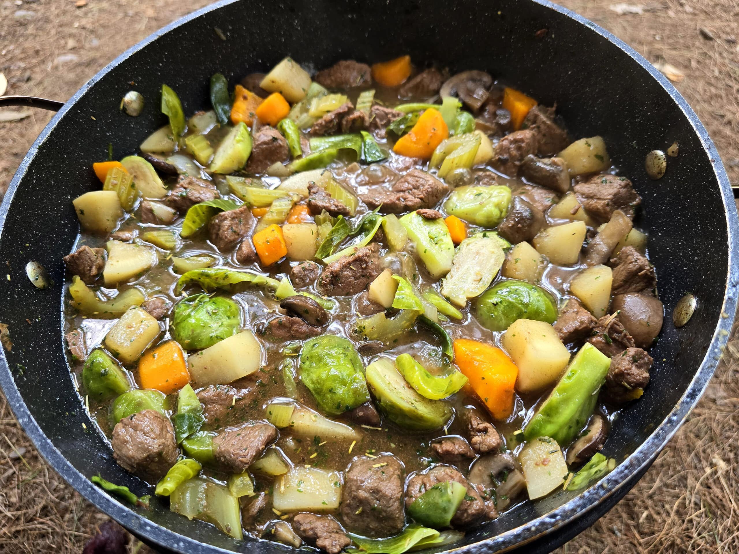 A large pot of campfire stew over a charcoal BBQ.