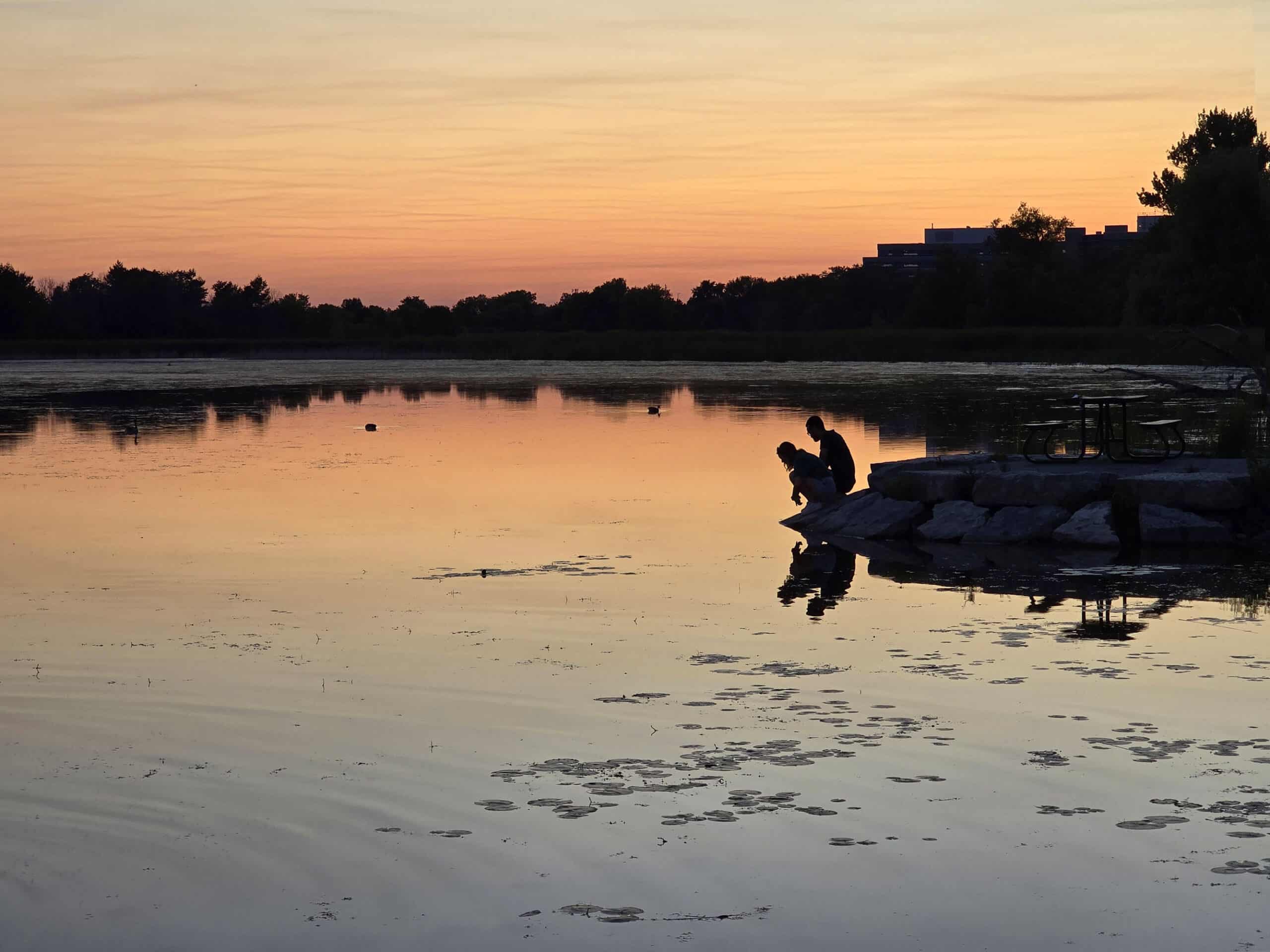 A couple on the shore of McLaughlin Bay in Darlington Provincial Park at sunset.