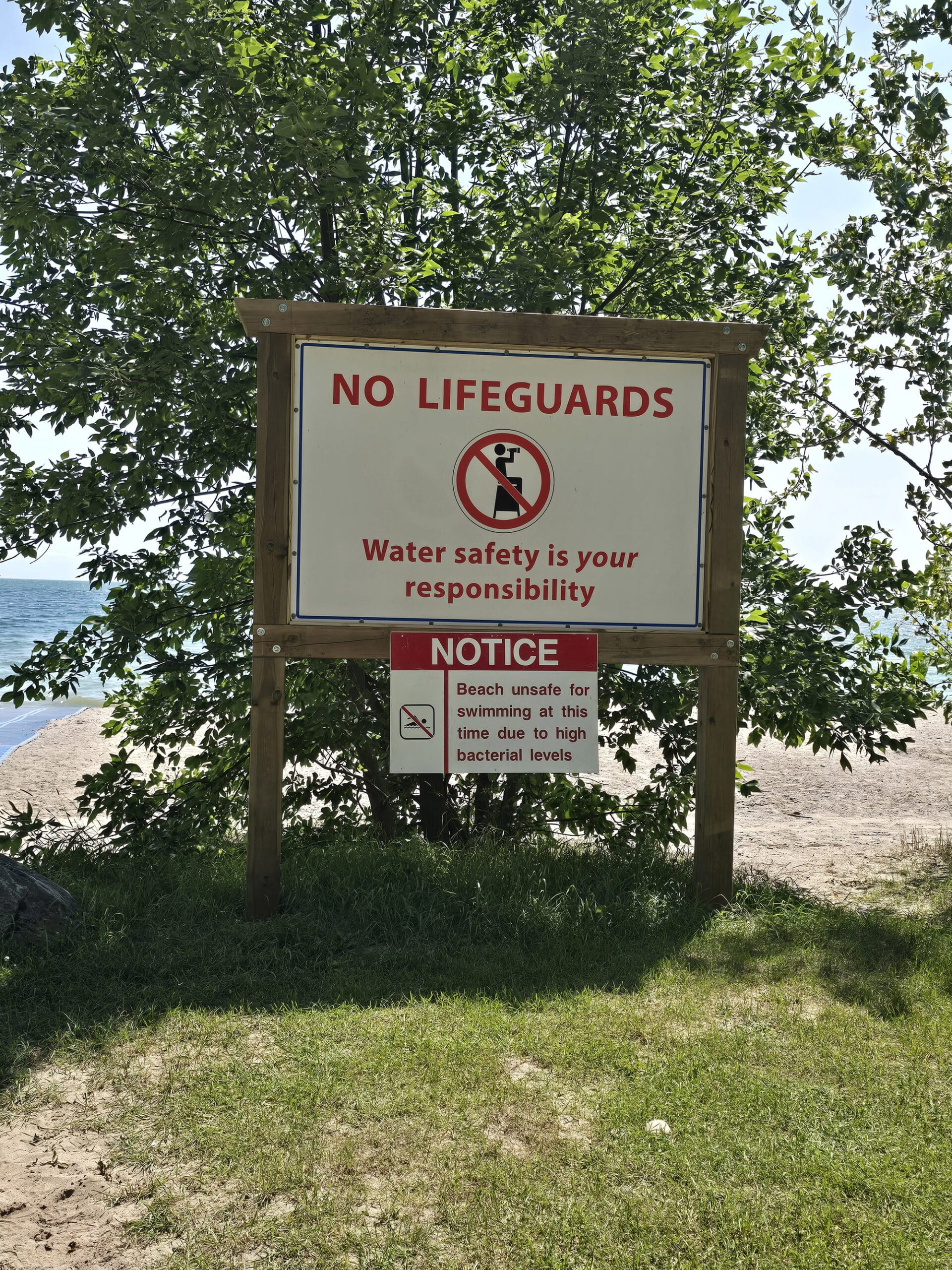 A sign saying that there's no lifeguards on duty, and that the water is unsafe due to bacteria levels.