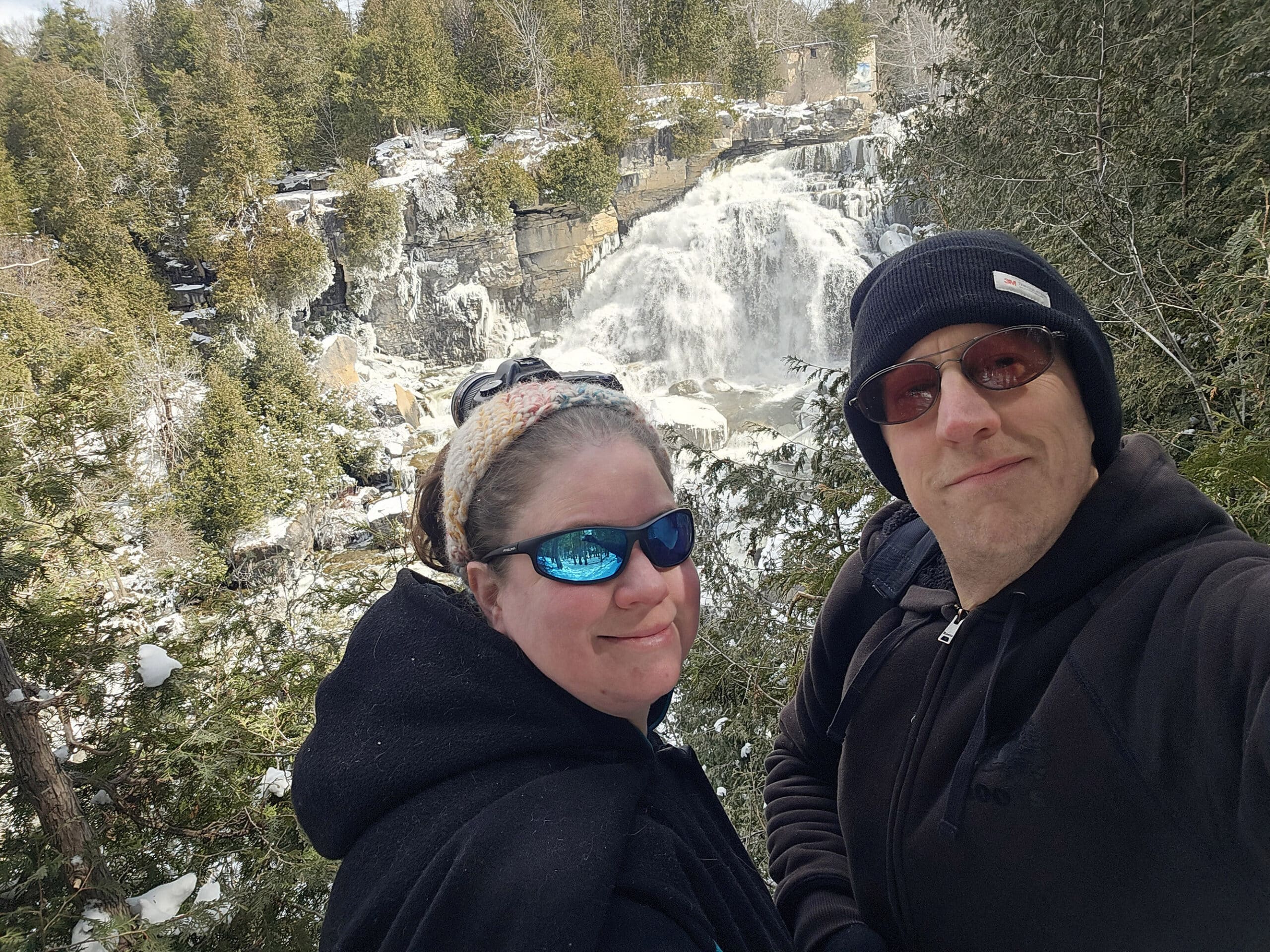 A middle aged white couple taking a winter selfie in front of Inglis Falls.