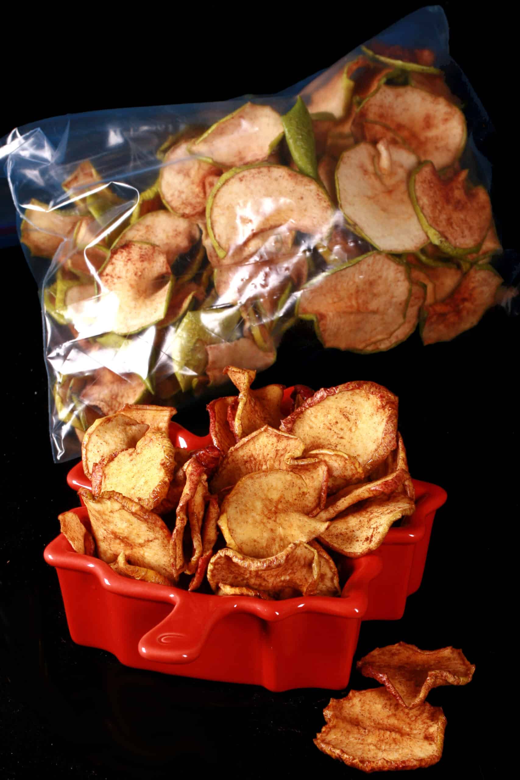 A bowl of maple cinnamon dehydrated apple slices in front of a bag of homemade apple chips.