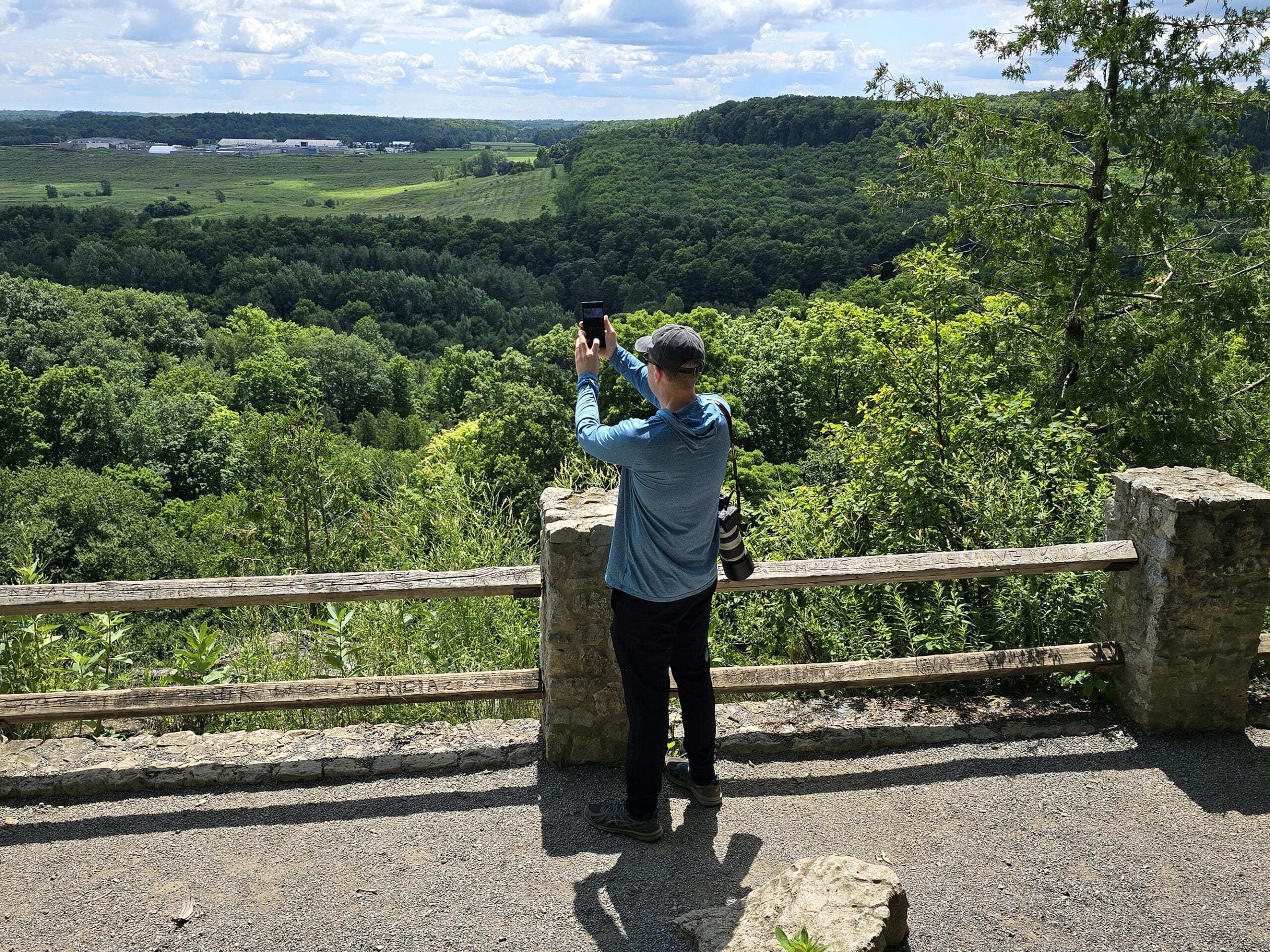 A middle aged white man taking a photo off the side of the Niagara Escarpment at Rattlesnake Point Conservation Area.