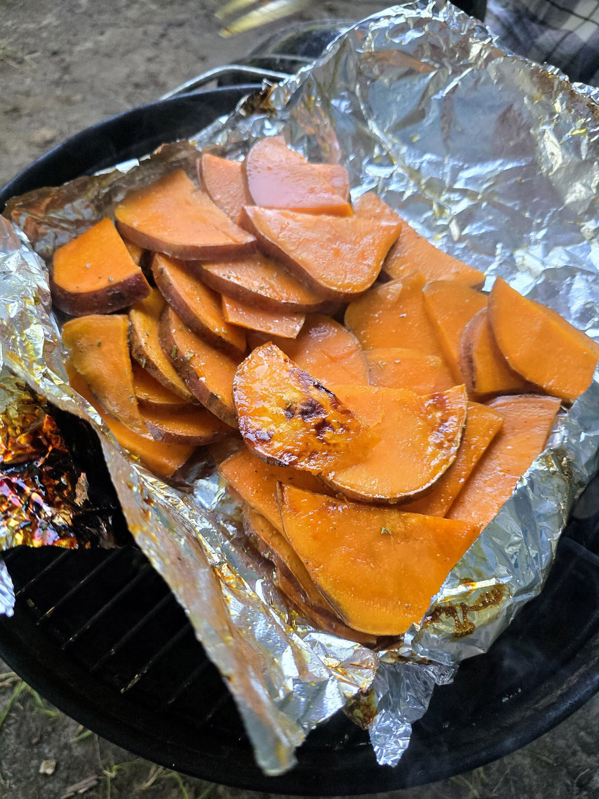 A foil packet of roasted sweet potatoes and maple syrup over a fire.