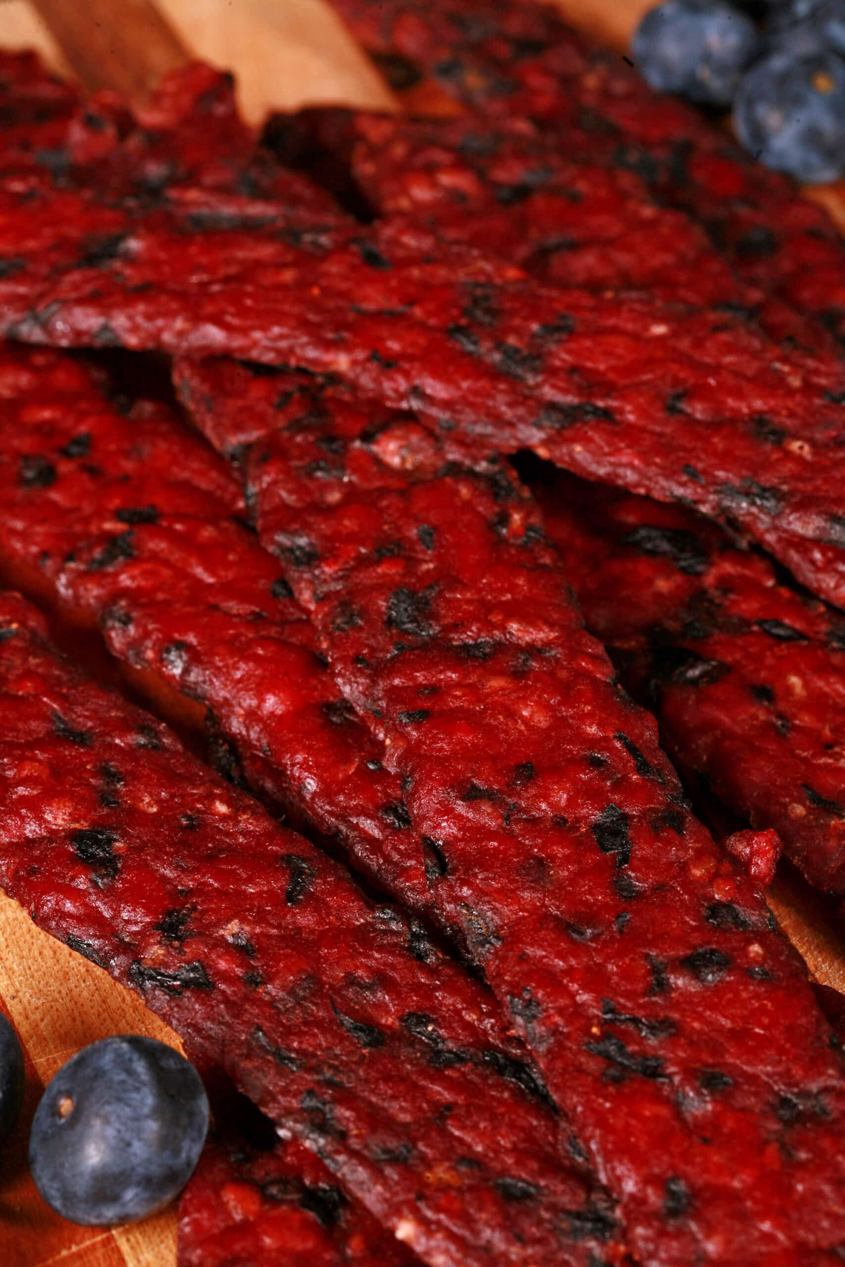 Several bison jerky strips on a cutting board with fresh blueberries.