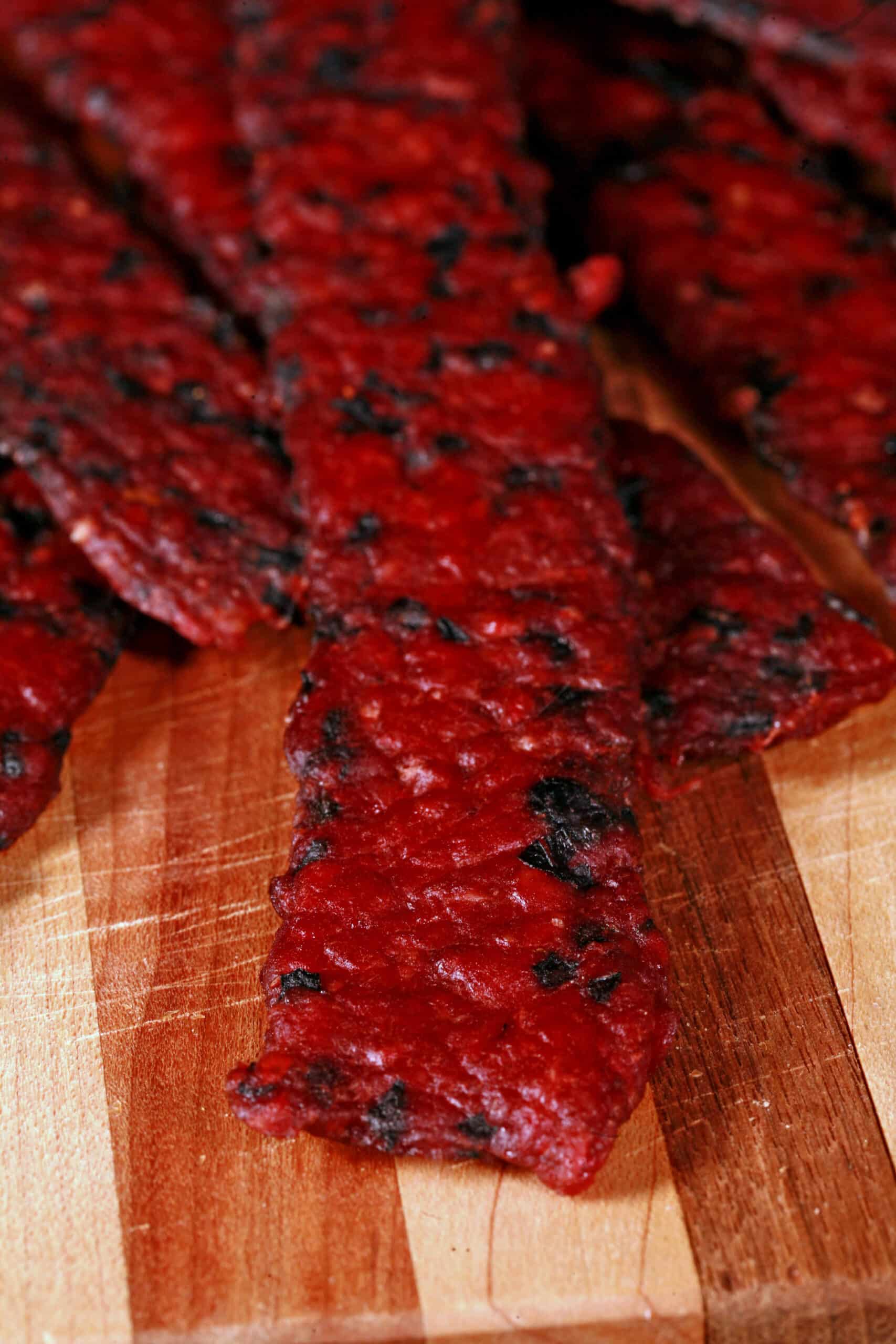 Several bison jerky strips on a cutting board with fresh blueberries.