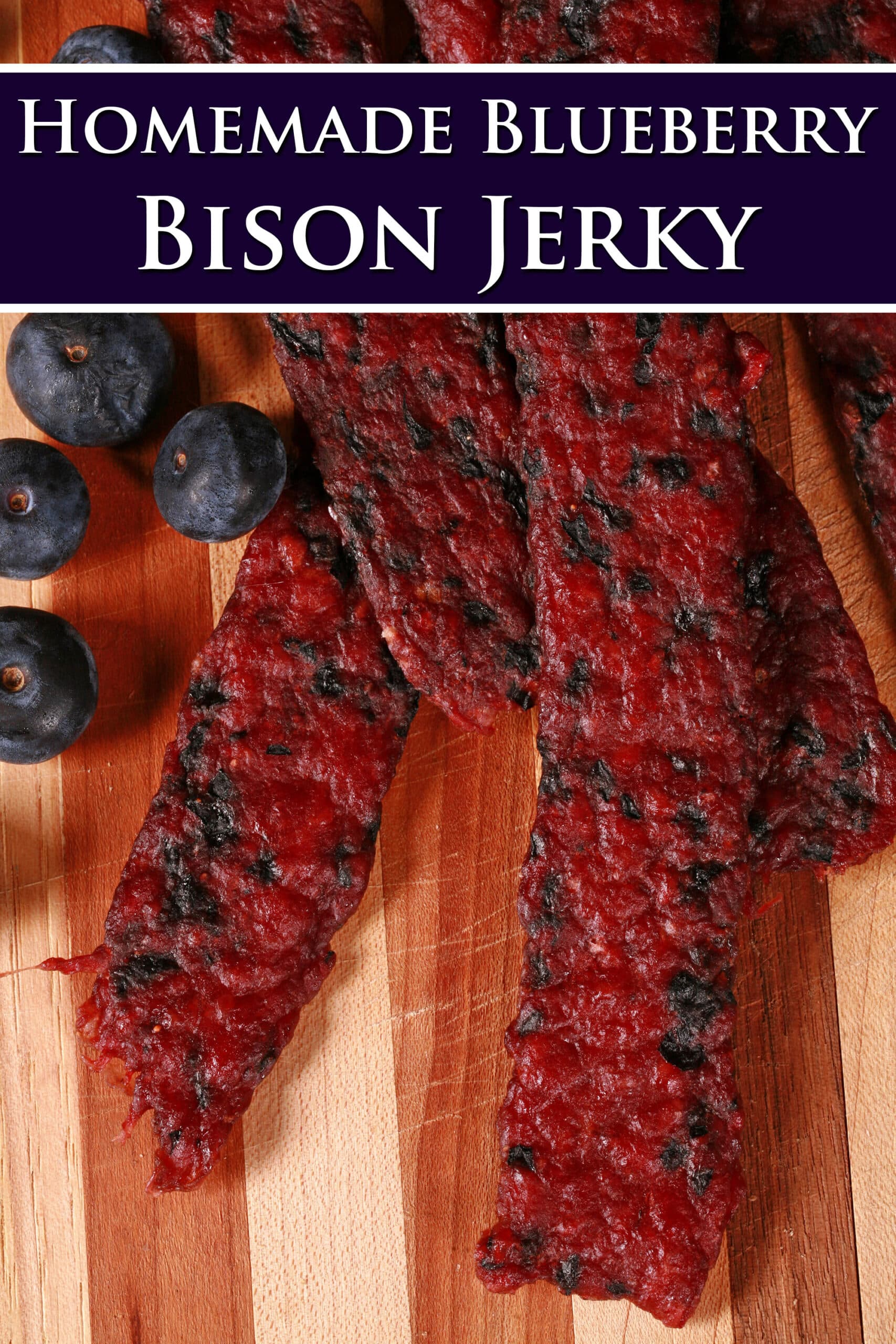 Several bison jerky strips on a cutting board with fresh blueberries. Overlaid text says blueberry bison jerky.