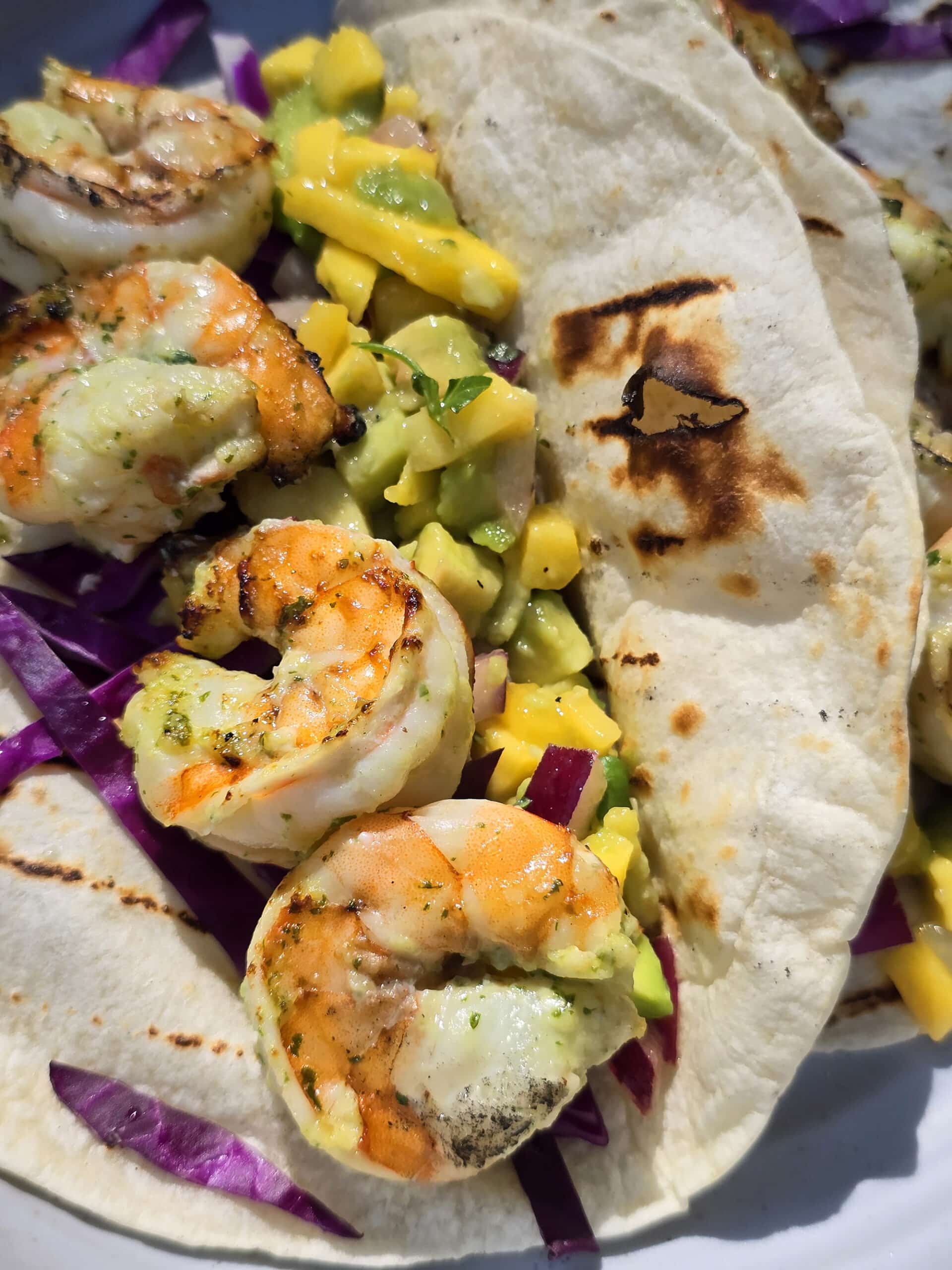 Two grilled shrimp tacos with mango salsa on a camping table.