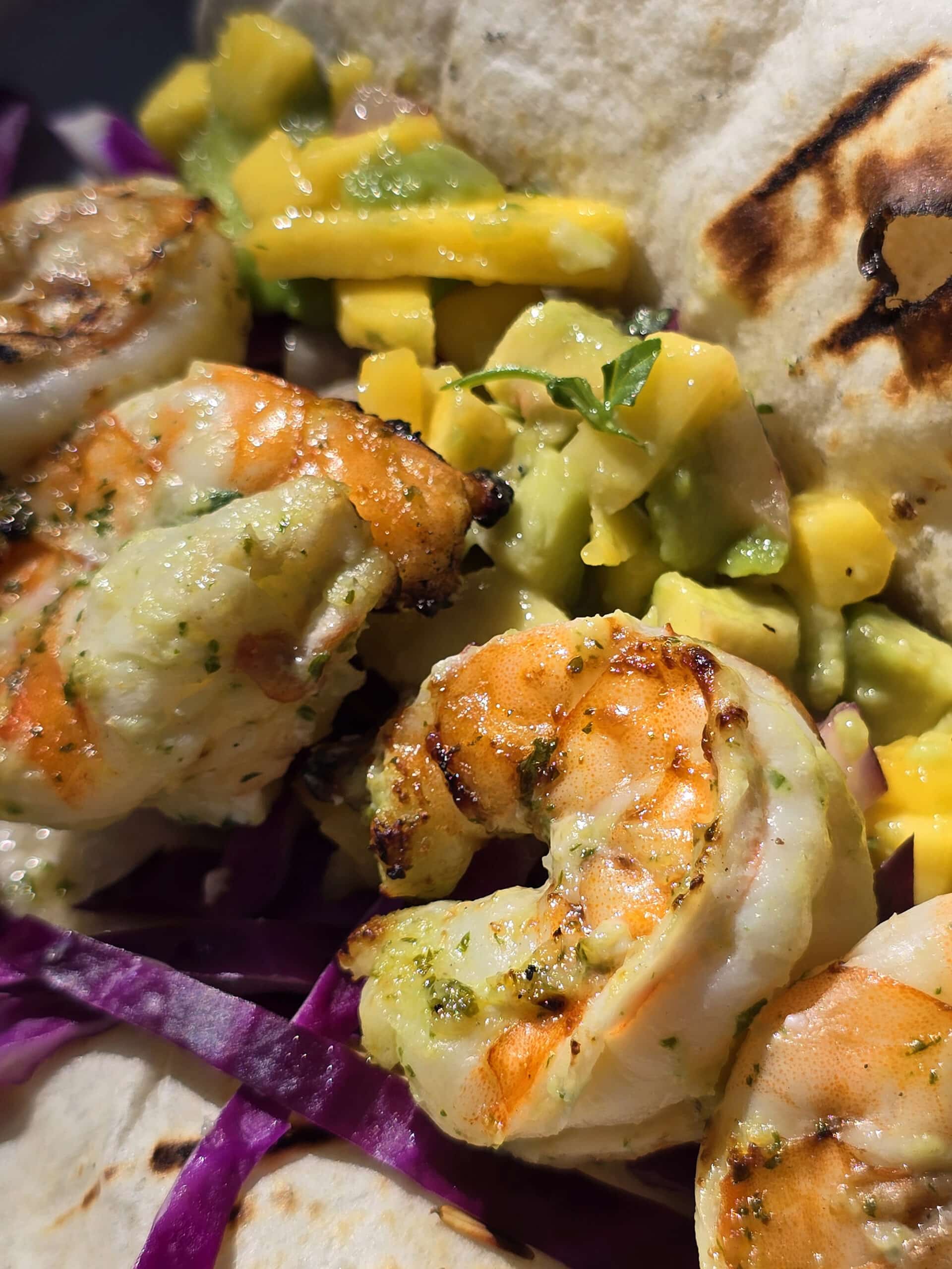 Two grilled shrimp tacos with mango salsa on a camping table.