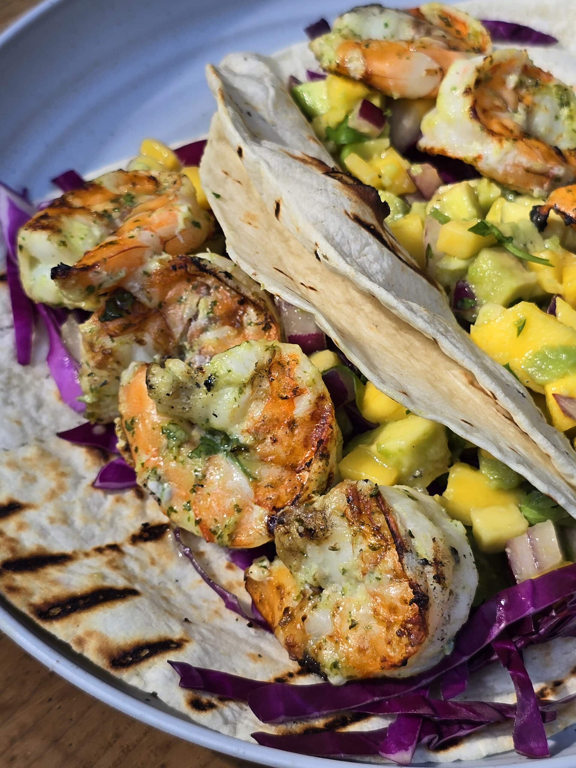 Two tacos with large grilled shrimp and mango salsa on a camping table.