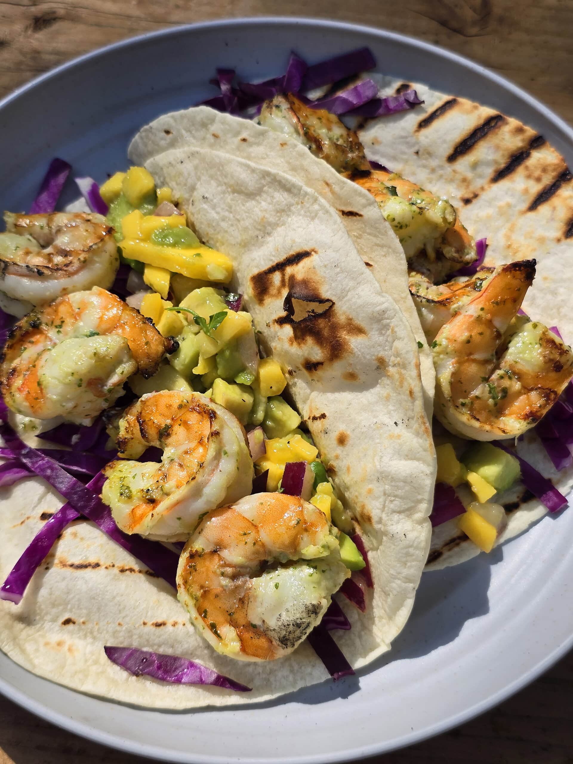 Two grilled shrimp tacos with mango salsa on a camping table.