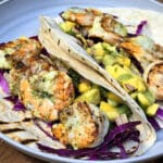 Two tacos with large grilled shrimp and mango salsa on a camping table.