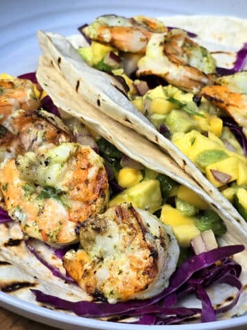 Two tacos with large grilled shrimp and mango salsa on a camping table.