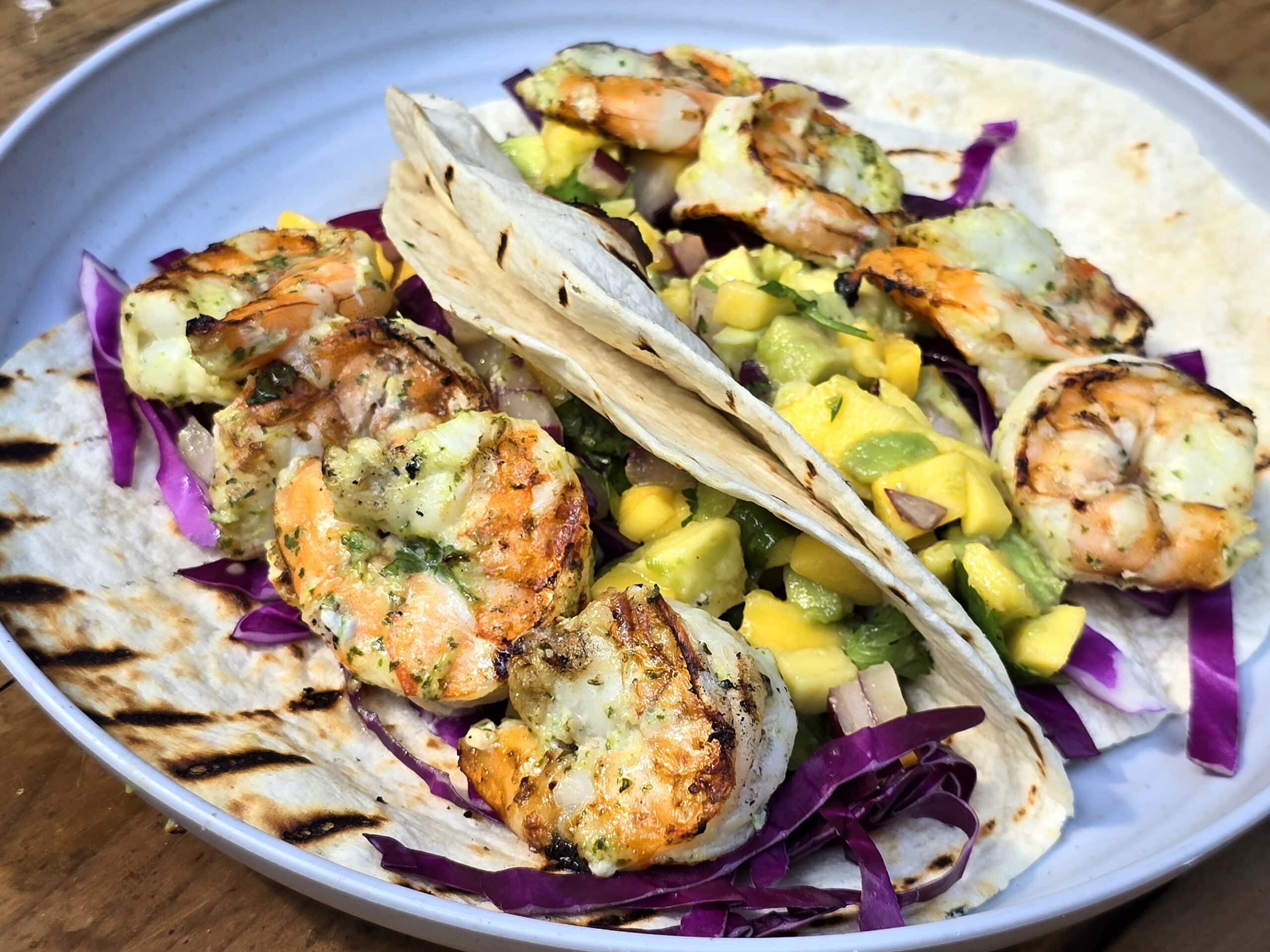 Two tacos with large grilled shrimp and mango salsa on a camping table.