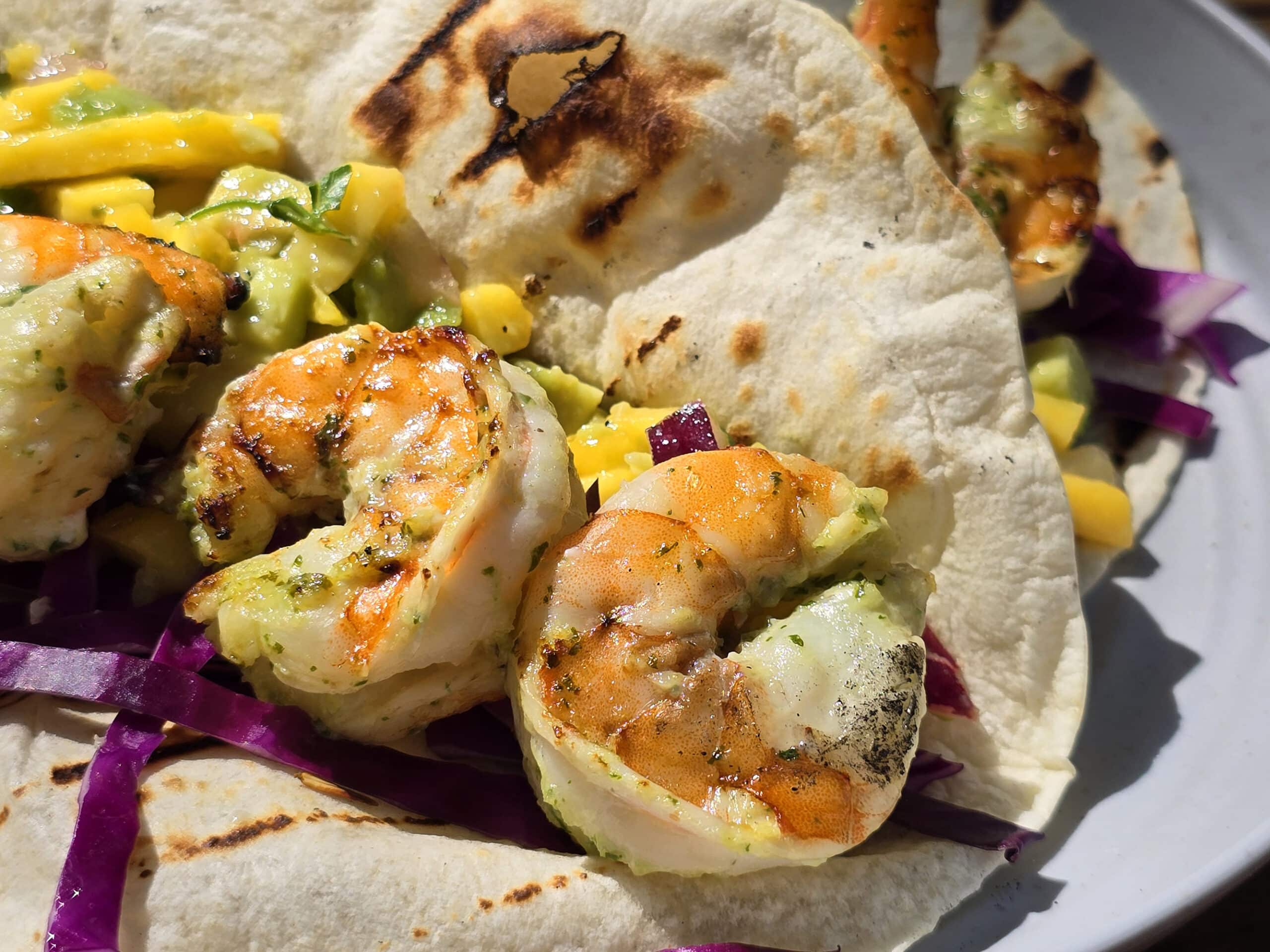 Two grilled shrimp tacos with mango salsa on a camping table.