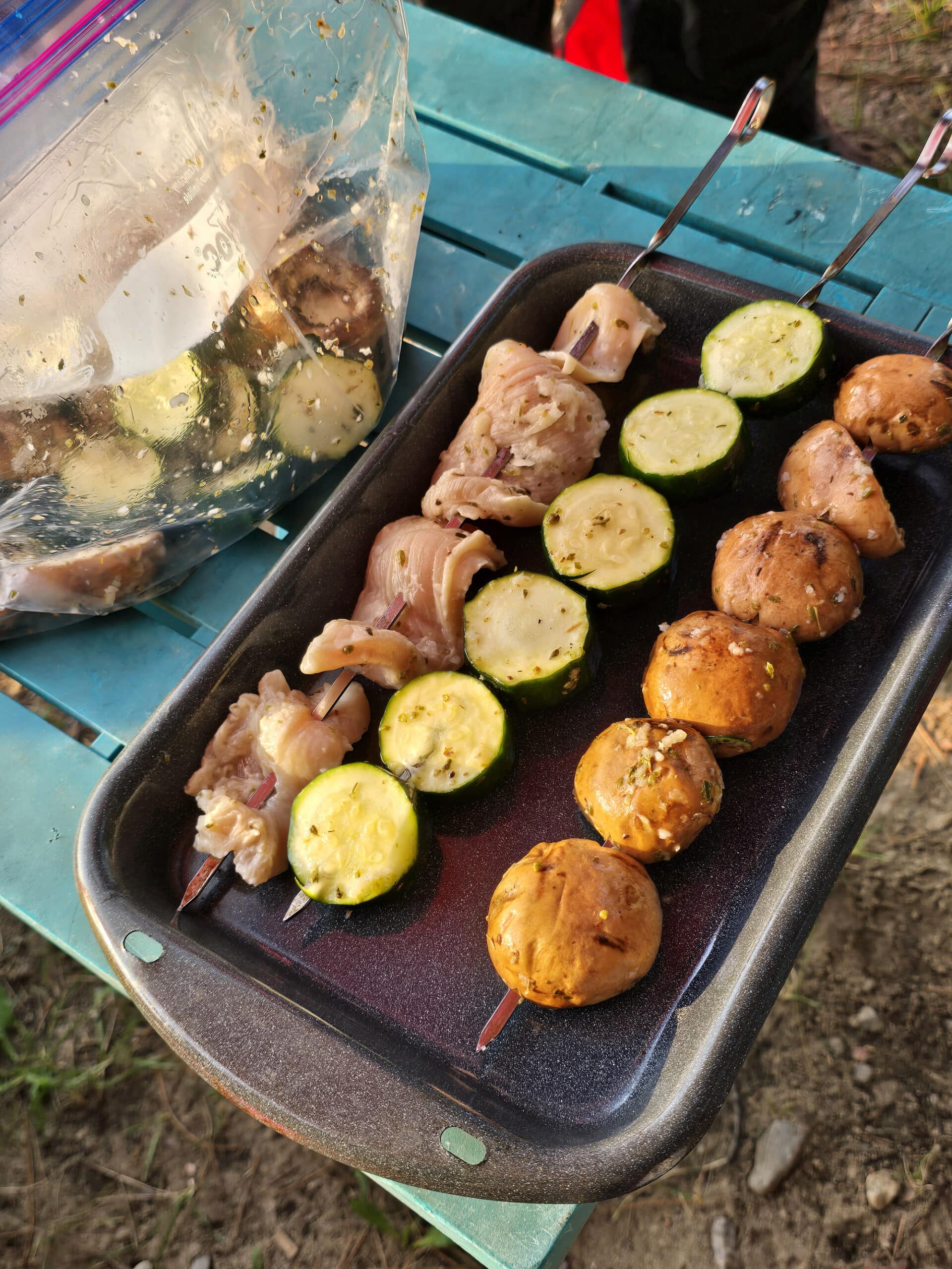 A tray of kebabs next to the bag of marinating chicken and vegetables.