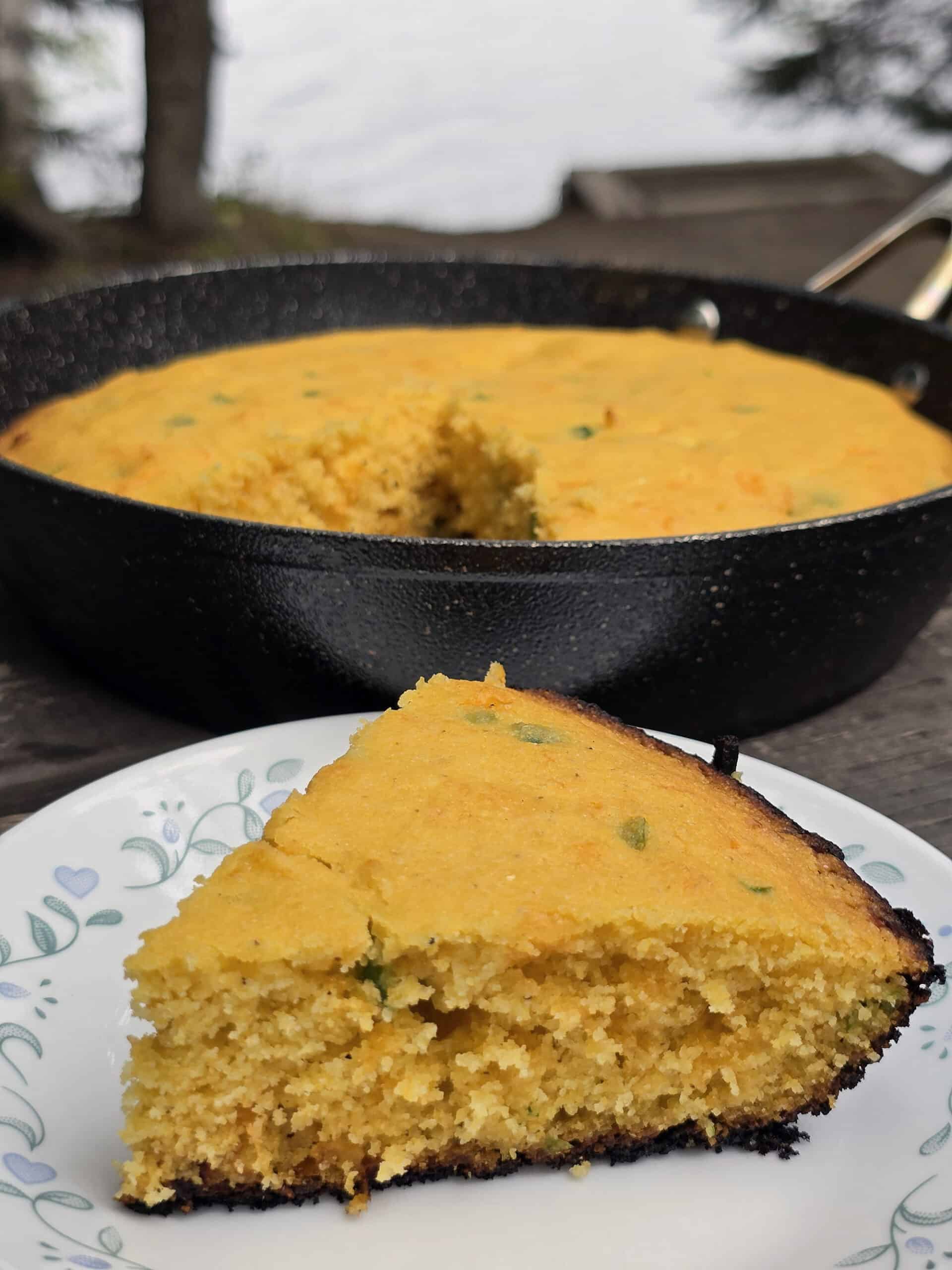 A pan and a slice of jalapeno cheddar cornbread on a picnic table.