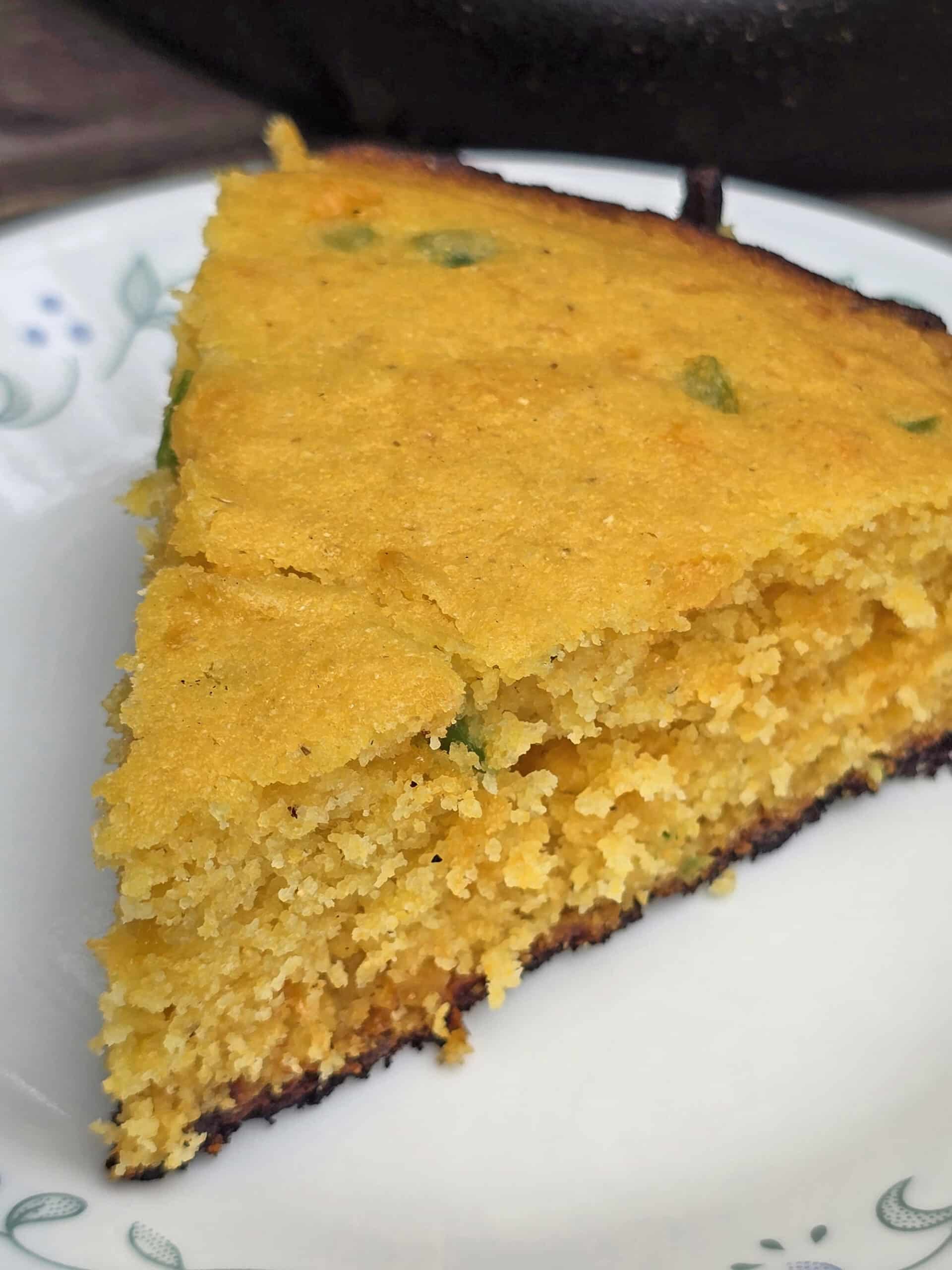 A close up slice of cheddar jalapeno cornbread on a picnic table.