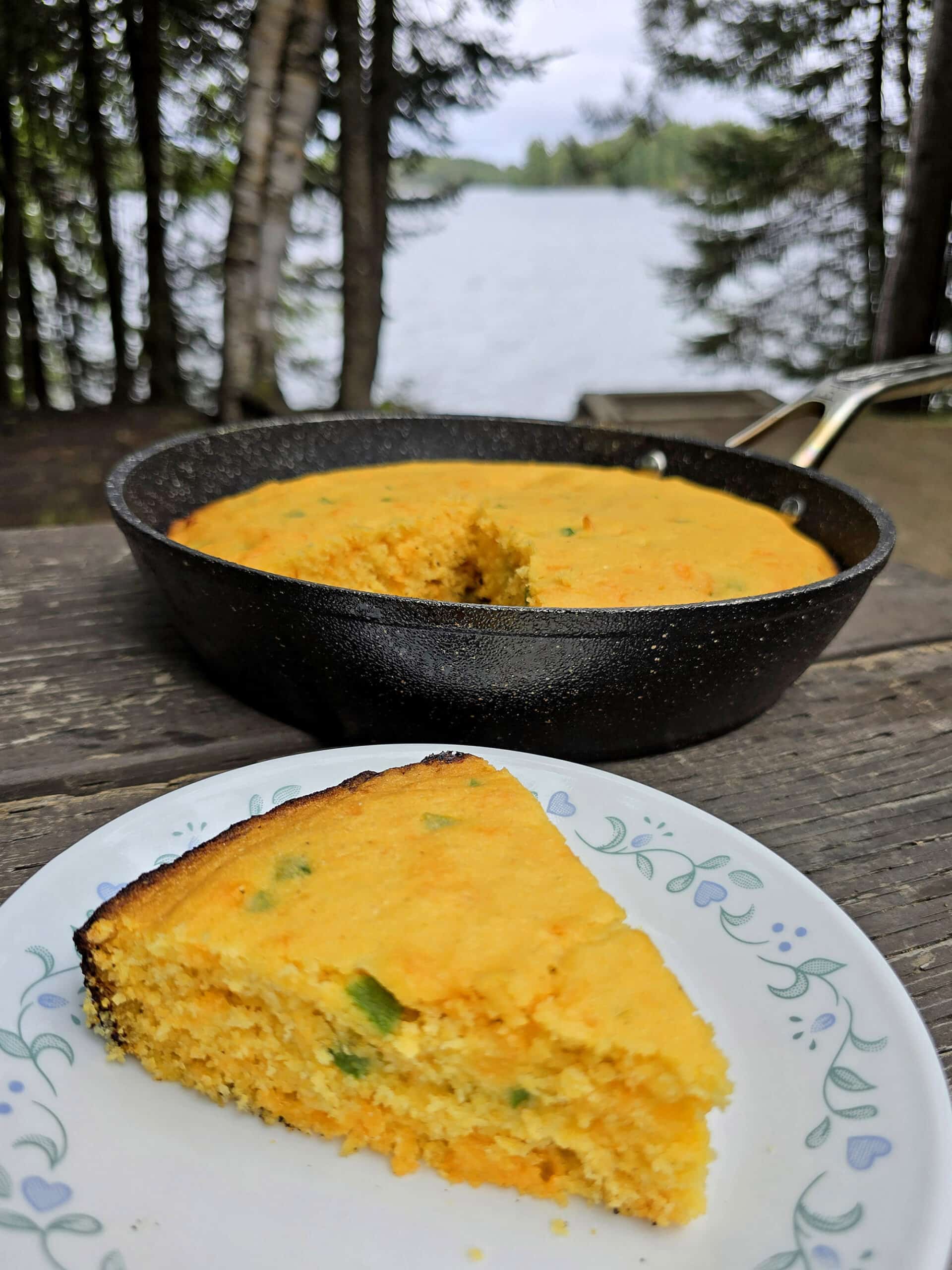 A pan and a slice of jalapeno cheddar cornbread on a picnic table.