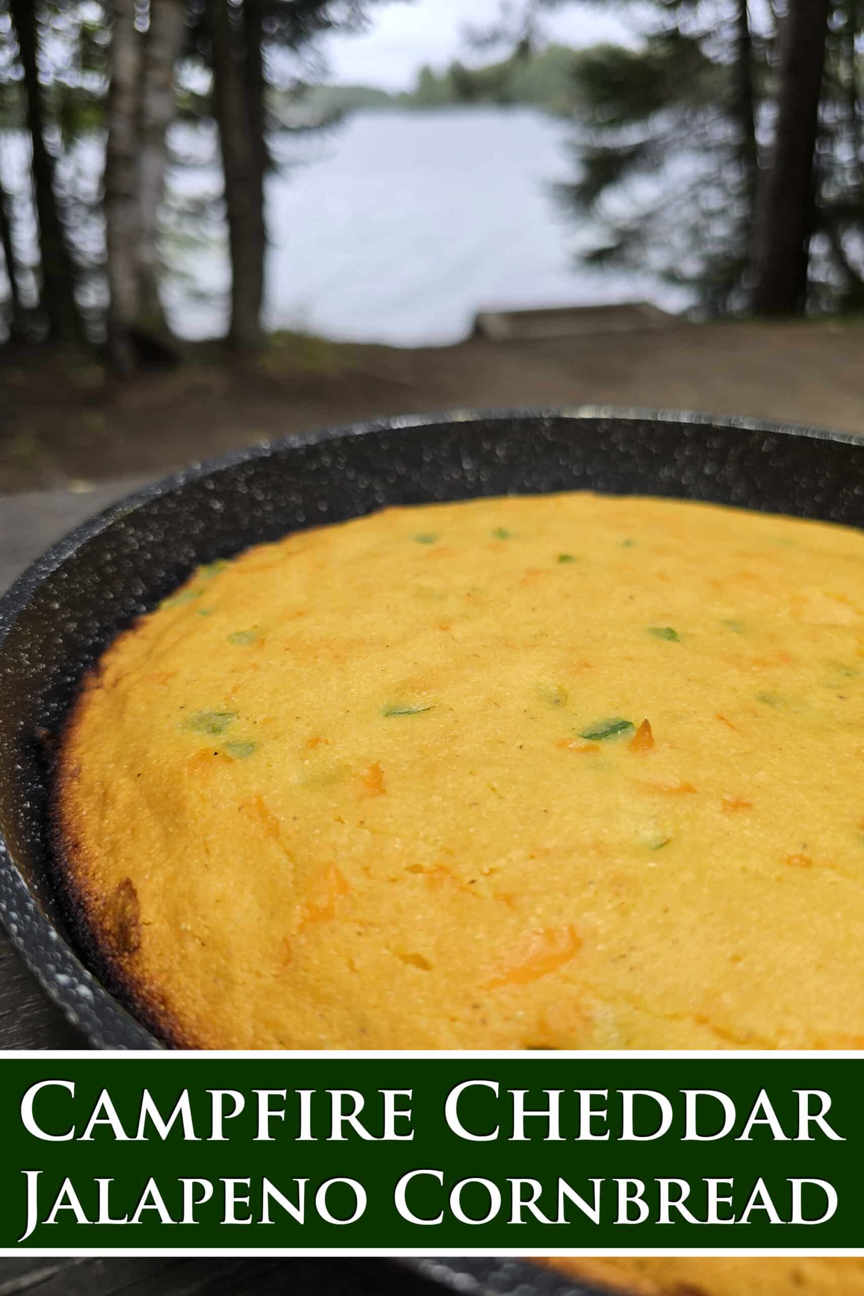 A pan of cheesy jalapeno cornbread on a picnic table.  Overlaid text says campfire cheddar jalapeno cornbread.