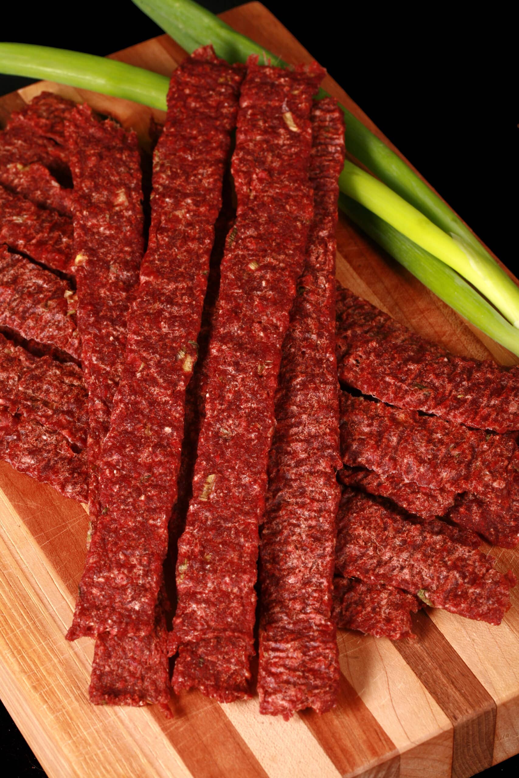 A pile of homemade ginger beef jerky on a wooden cutting board with green onions.