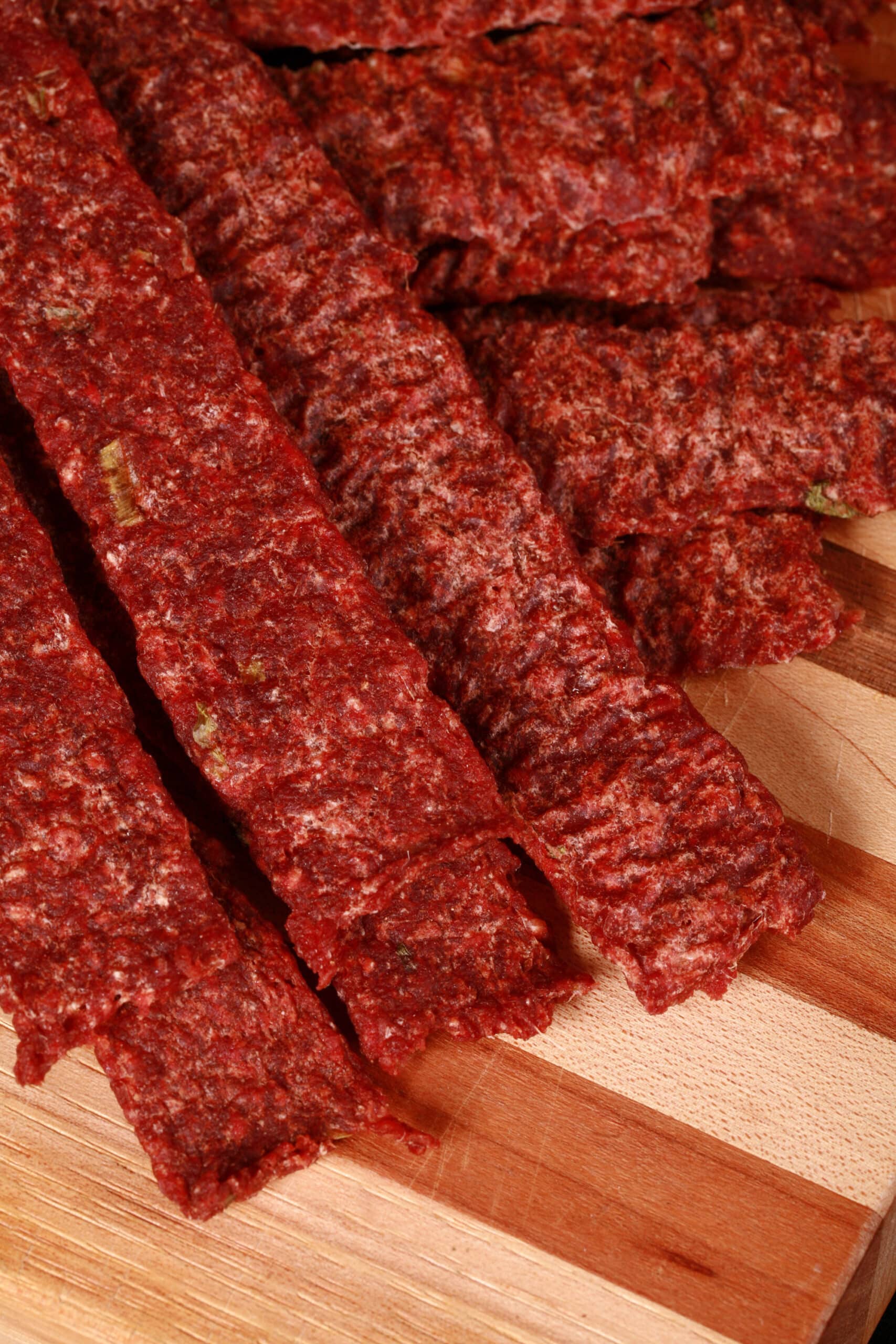 A pile of homemade ginger ground beef jerky on a wooden cutting board with green onions.