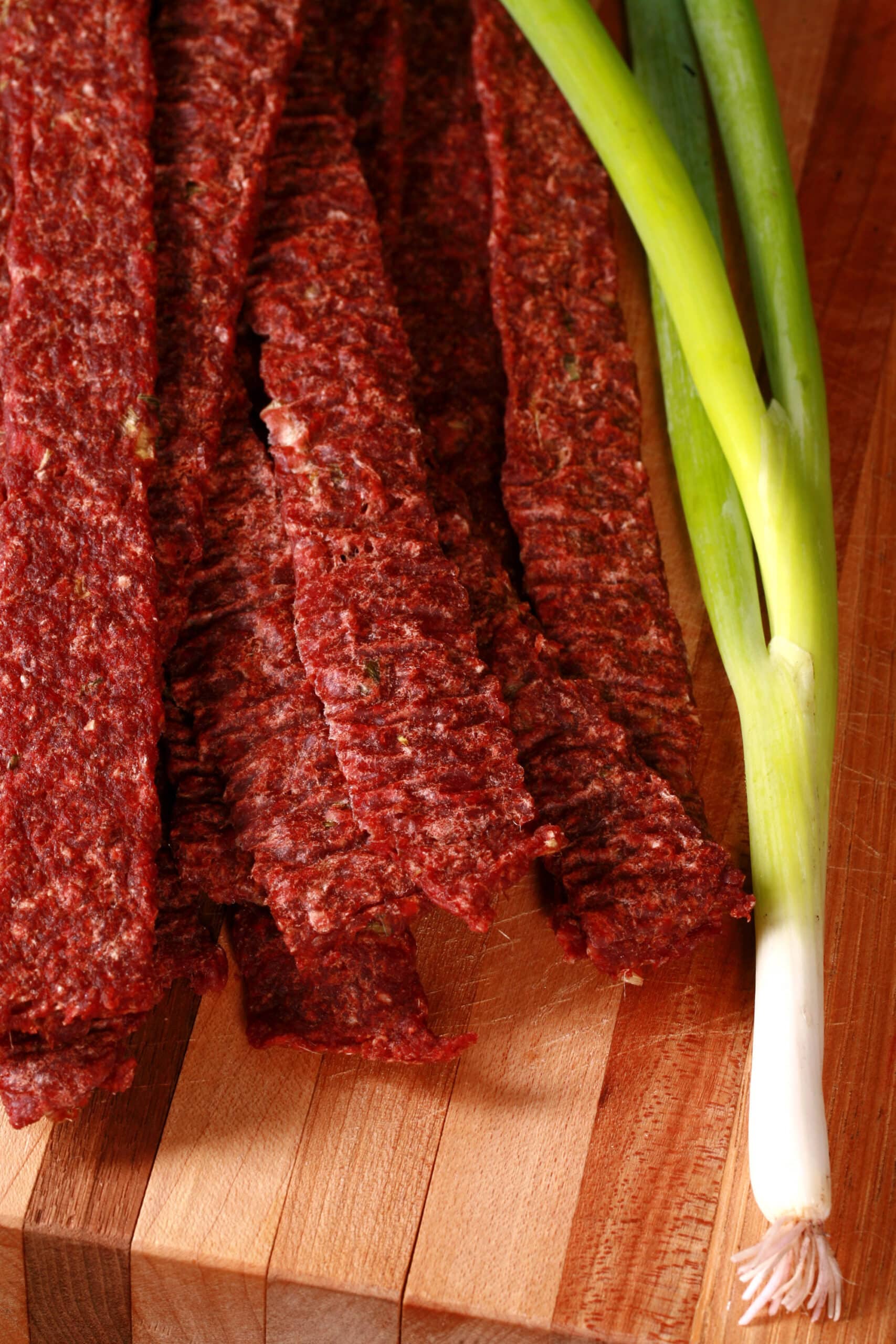 A pile of homemade ginger beef jerky on a wooden cutting board with green onions.