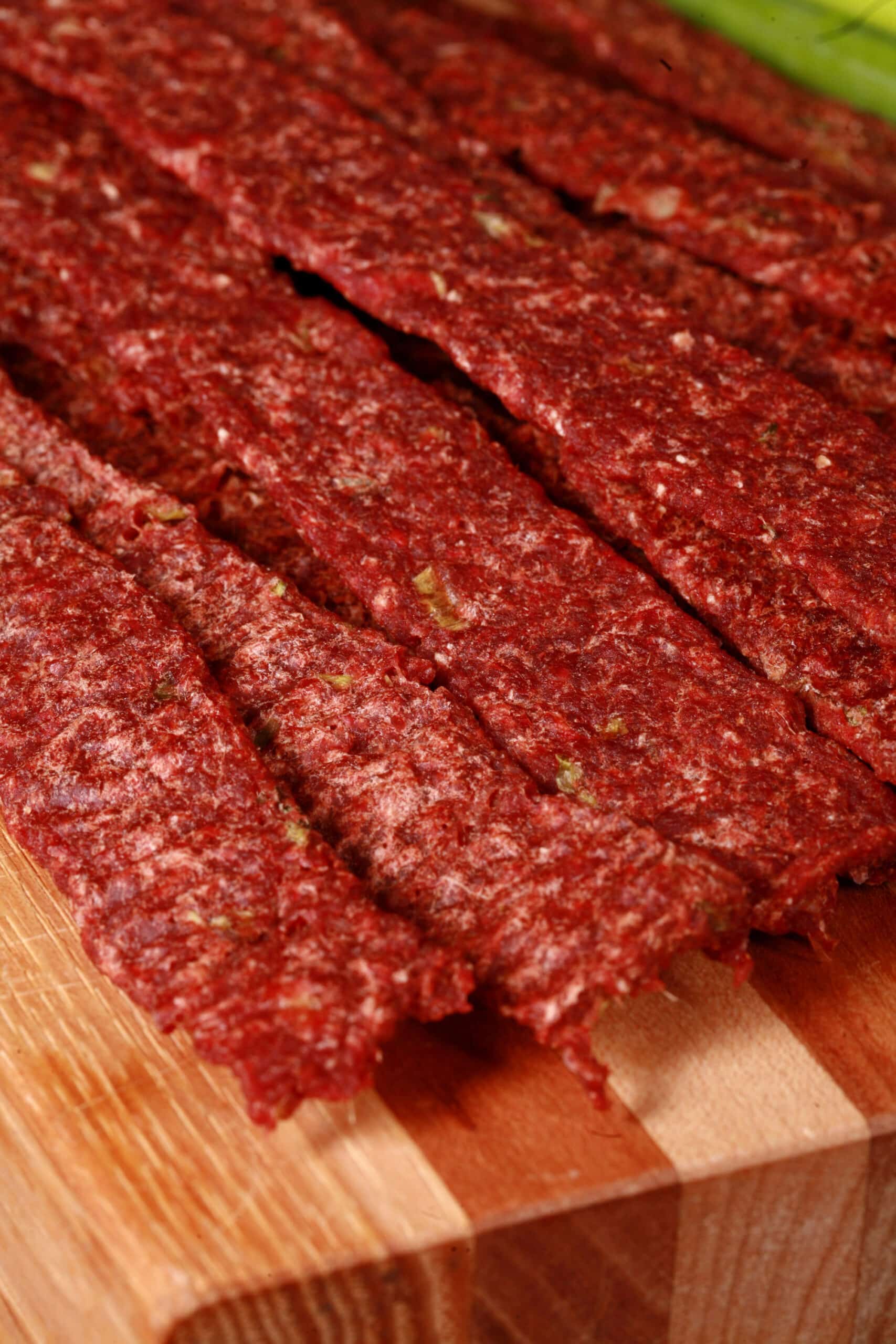 A pile of homemade ginger beef jerky on a wooden cutting board with green onions.