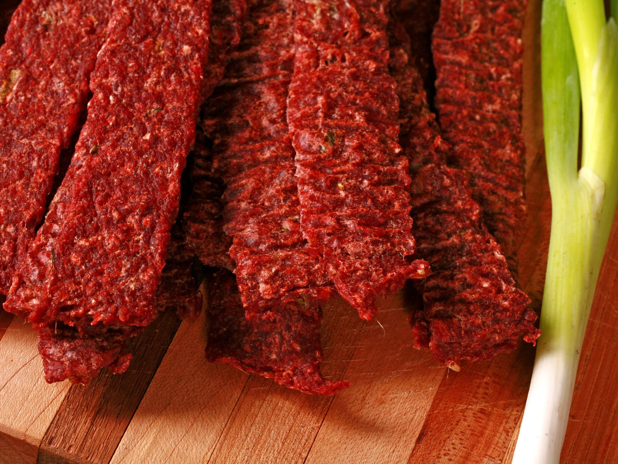 A pile of homemade ginger ground beef jerky on a wooden cutting board with green onions.