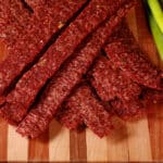 A pile of homemade ginger beef jerky on a wooden cutting board with green onions.