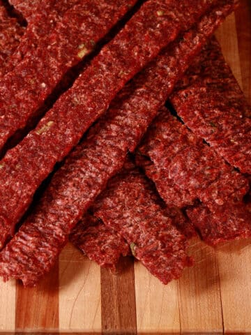 A pile of homemade ginger beef jerky on a wooden cutting board with green onions.