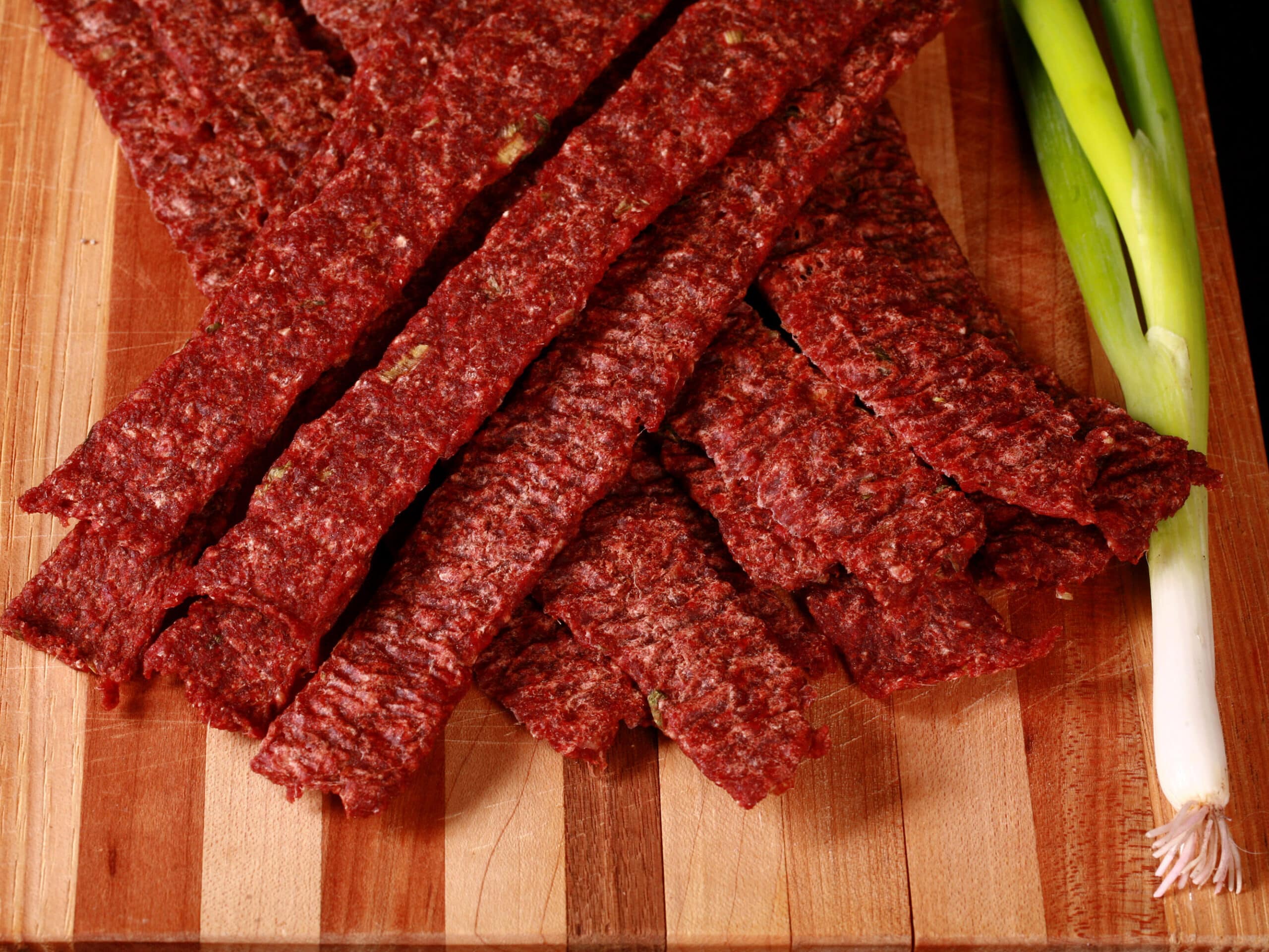 A pile of homemade ginger beef jerky on a wooden cutting board with green onions.