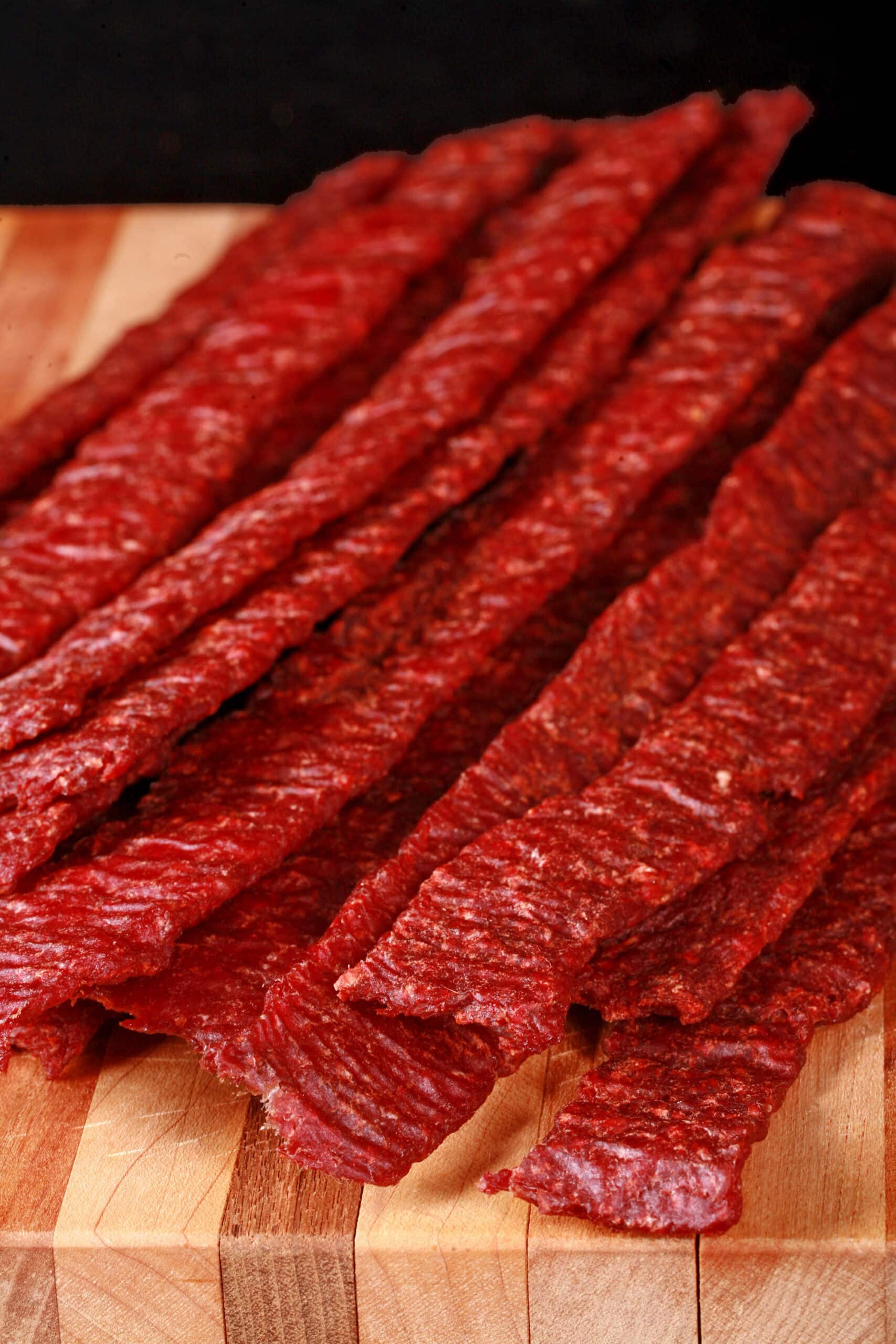 A pile of homemade ground beef jerky strips on a wooden cutting board.