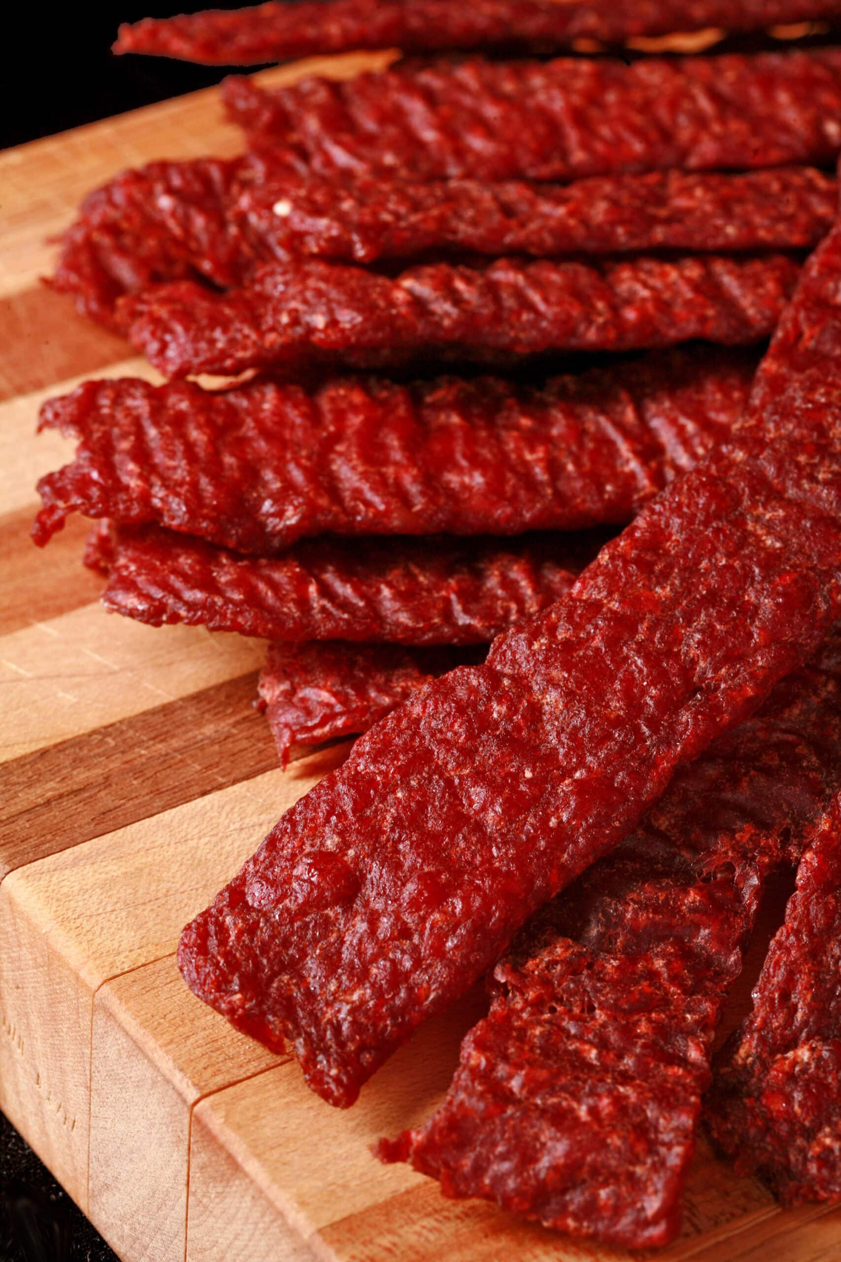 A pile of homemade ground beef jerky strips on a wooden cutting board.