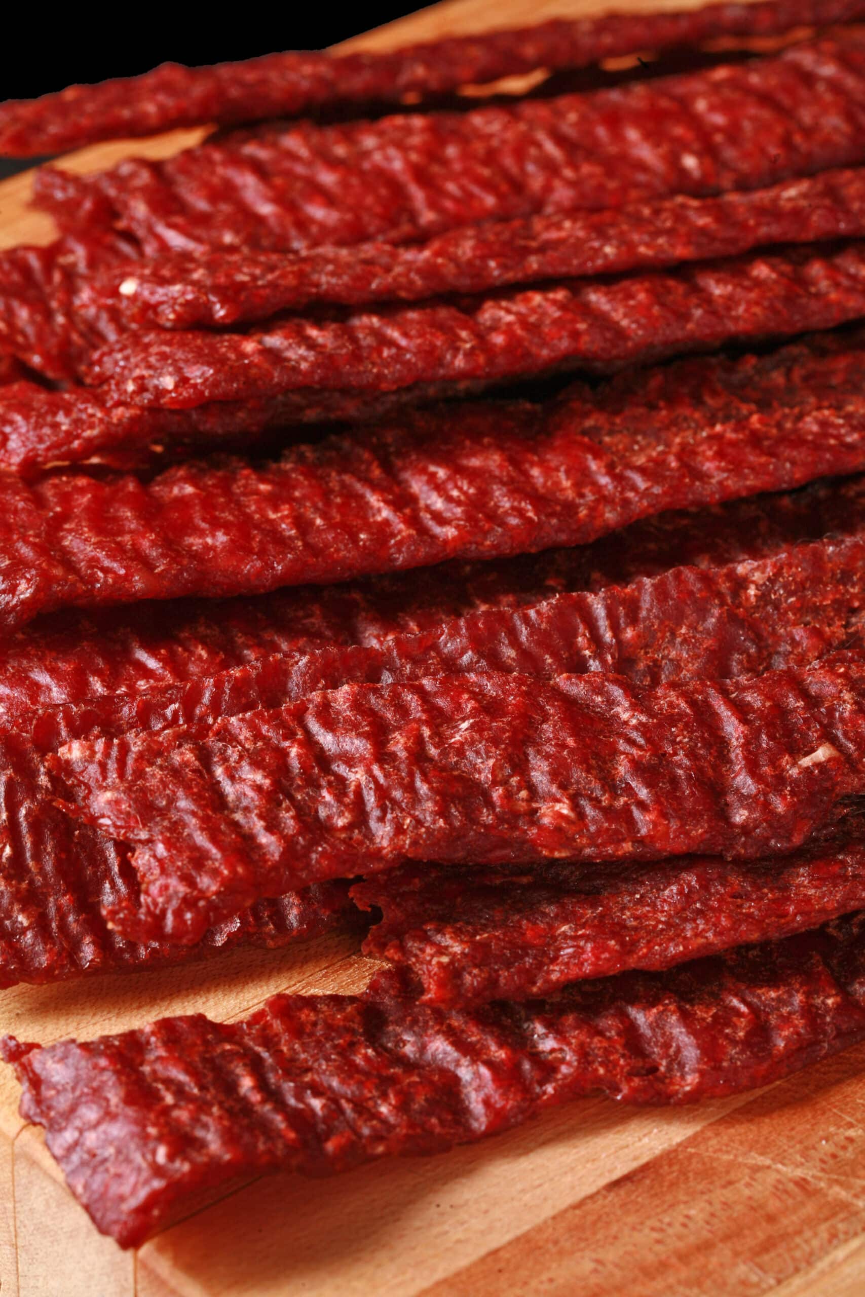 A pile of homemade ground beef jerky strips on a wooden cutting board.