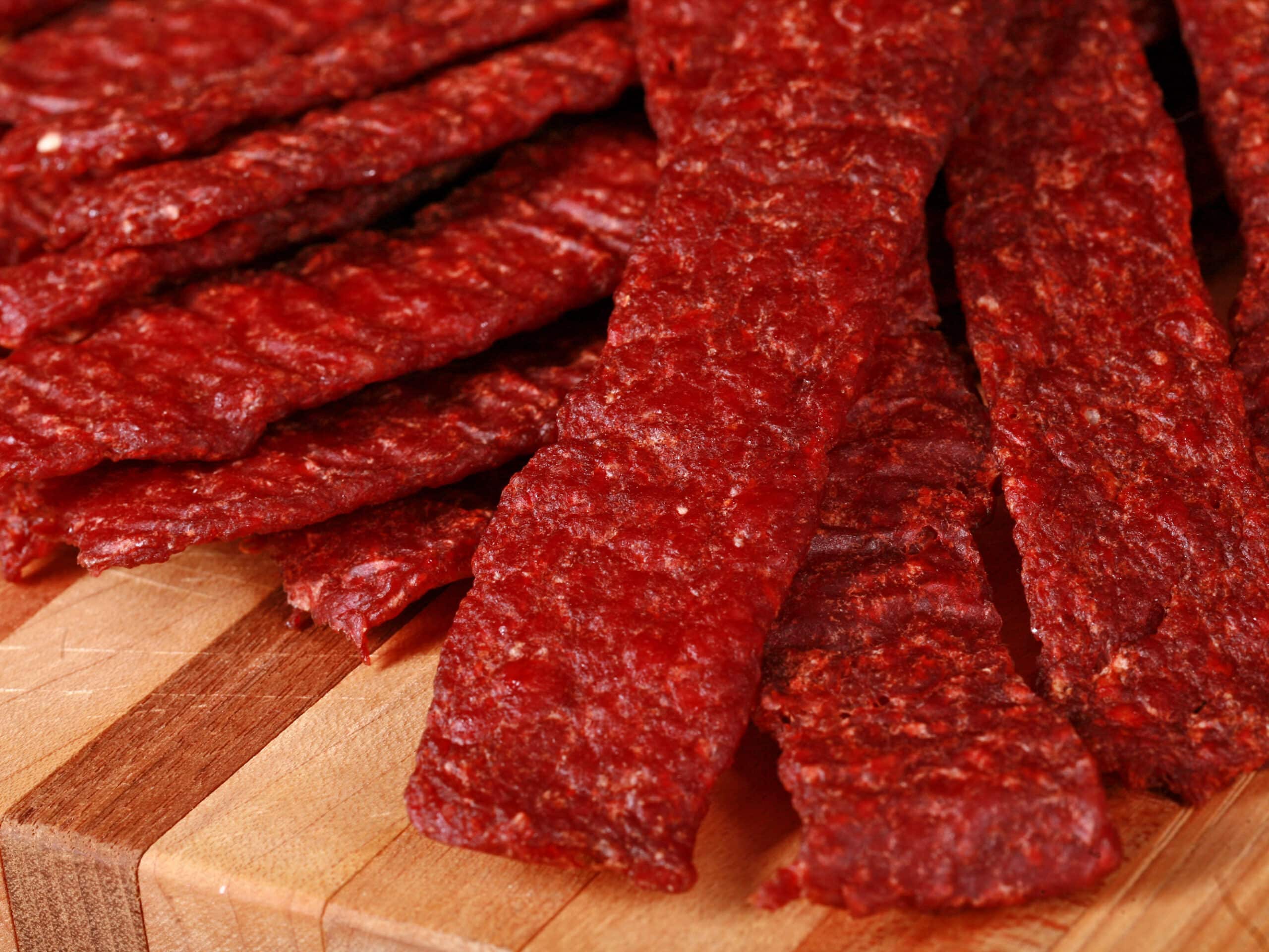 A pile of homemade ground beef jerky strips on a wooden cutting board.