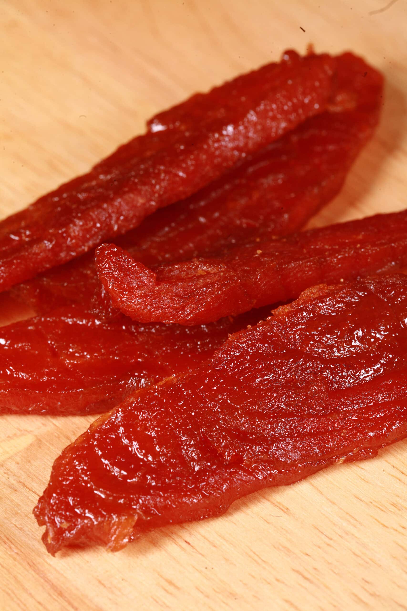 A pile of homemade maple salmon jerky on a wooden cutting board.