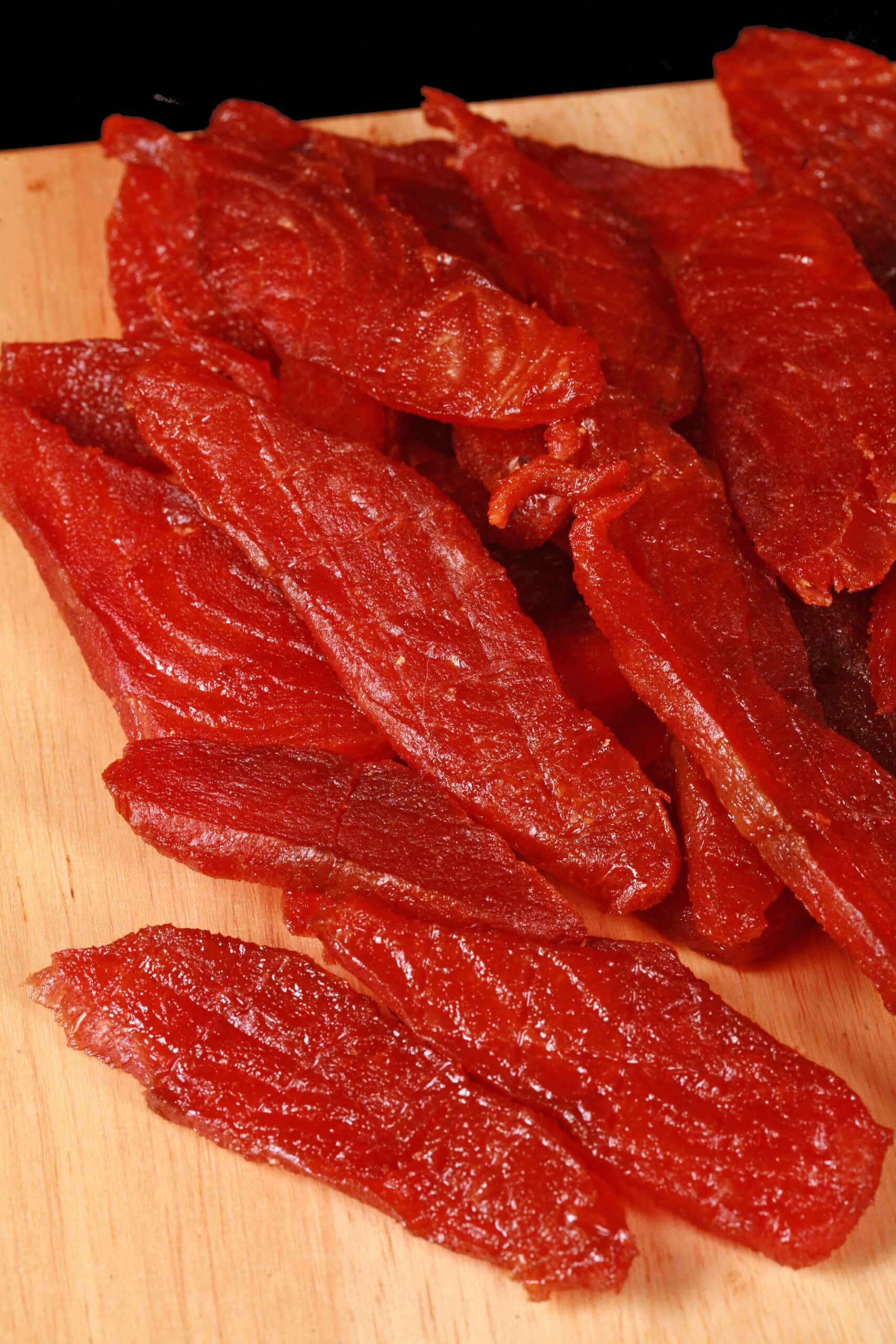 A pile of homemade salmon jerky on a wooden cutting board.