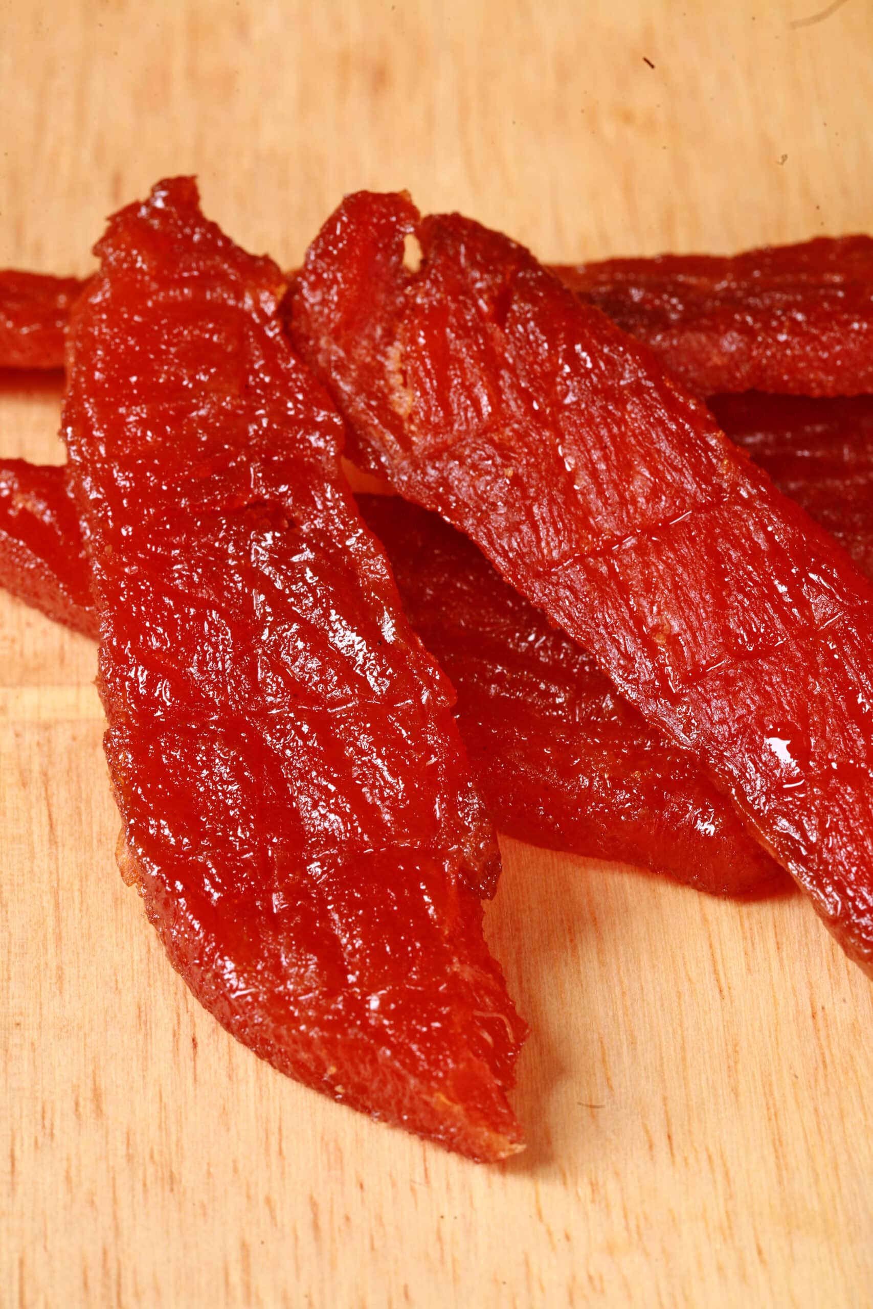 A pile of homemade maple salmon jerky on a wooden cutting board.