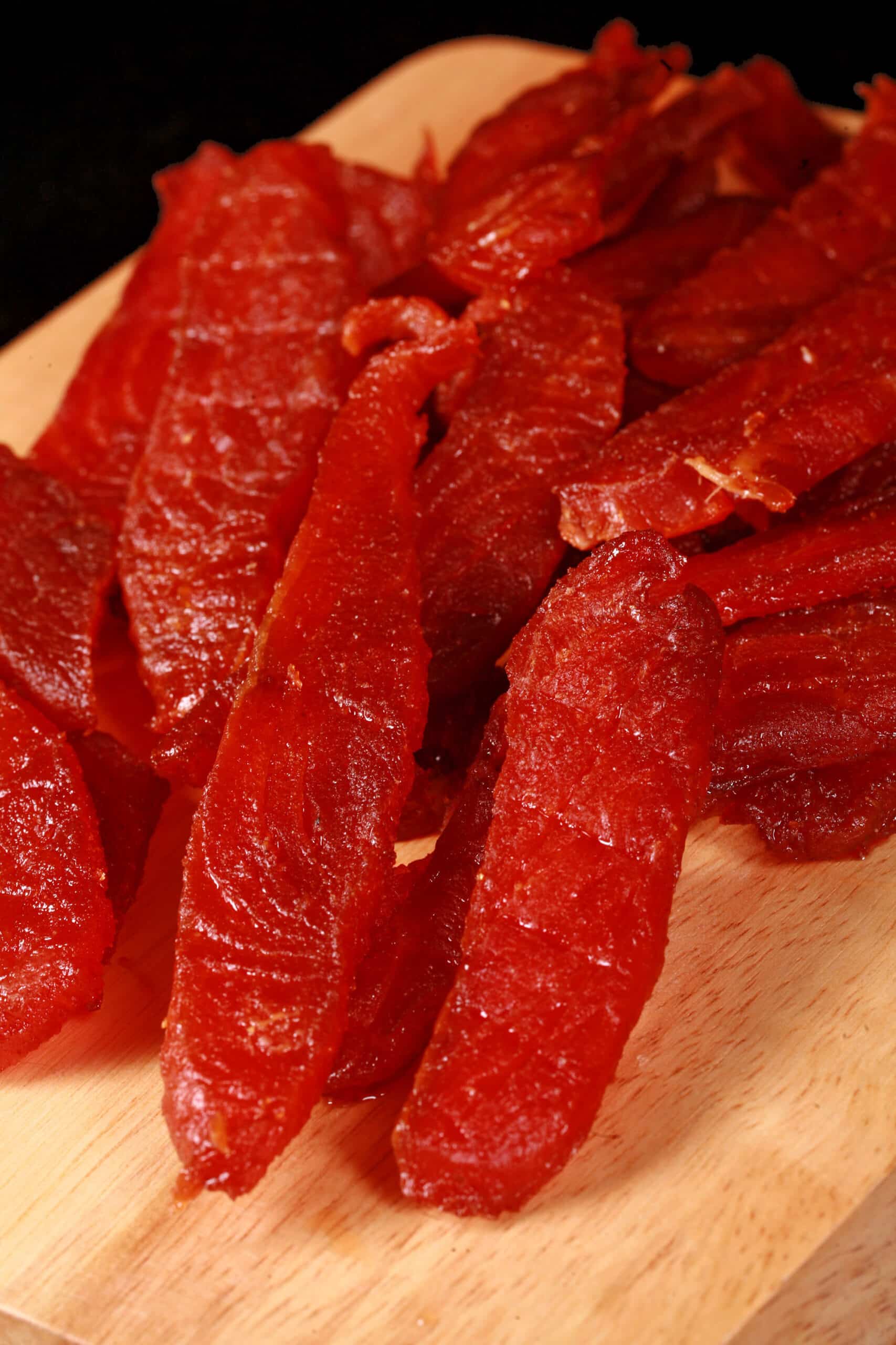 A pile of homemade salmon jerky on a wooden cutting board.