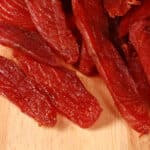 A pile of homemade salmon jerky on a wooden cutting board.